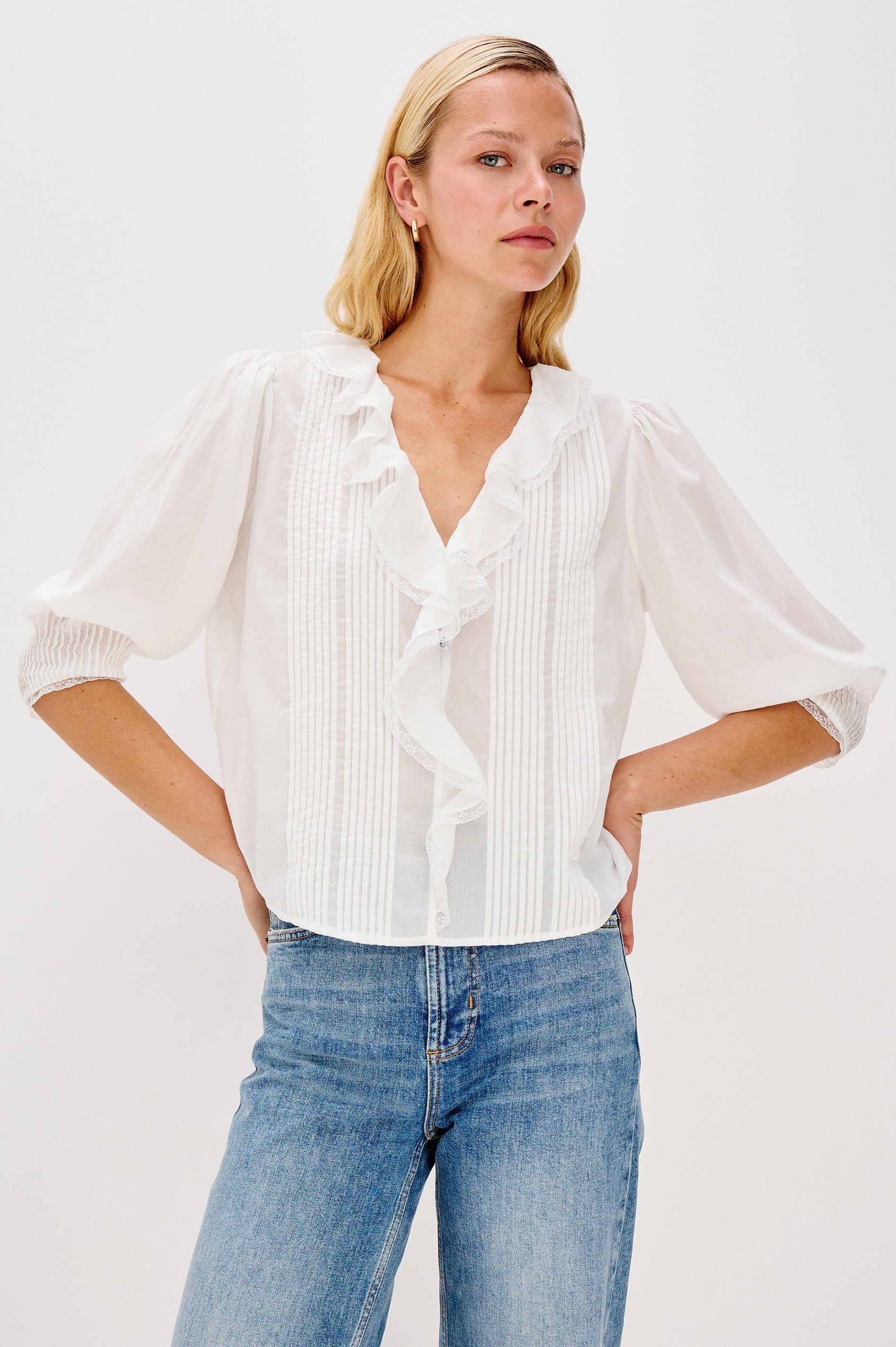 A relaxed-fit cotton blouse with cascading ruffles down the front in White Colorway. The blouse is accented with lace trim at the neckline and cuffs, adding a romantic, feminine touch. Front view featured on model.