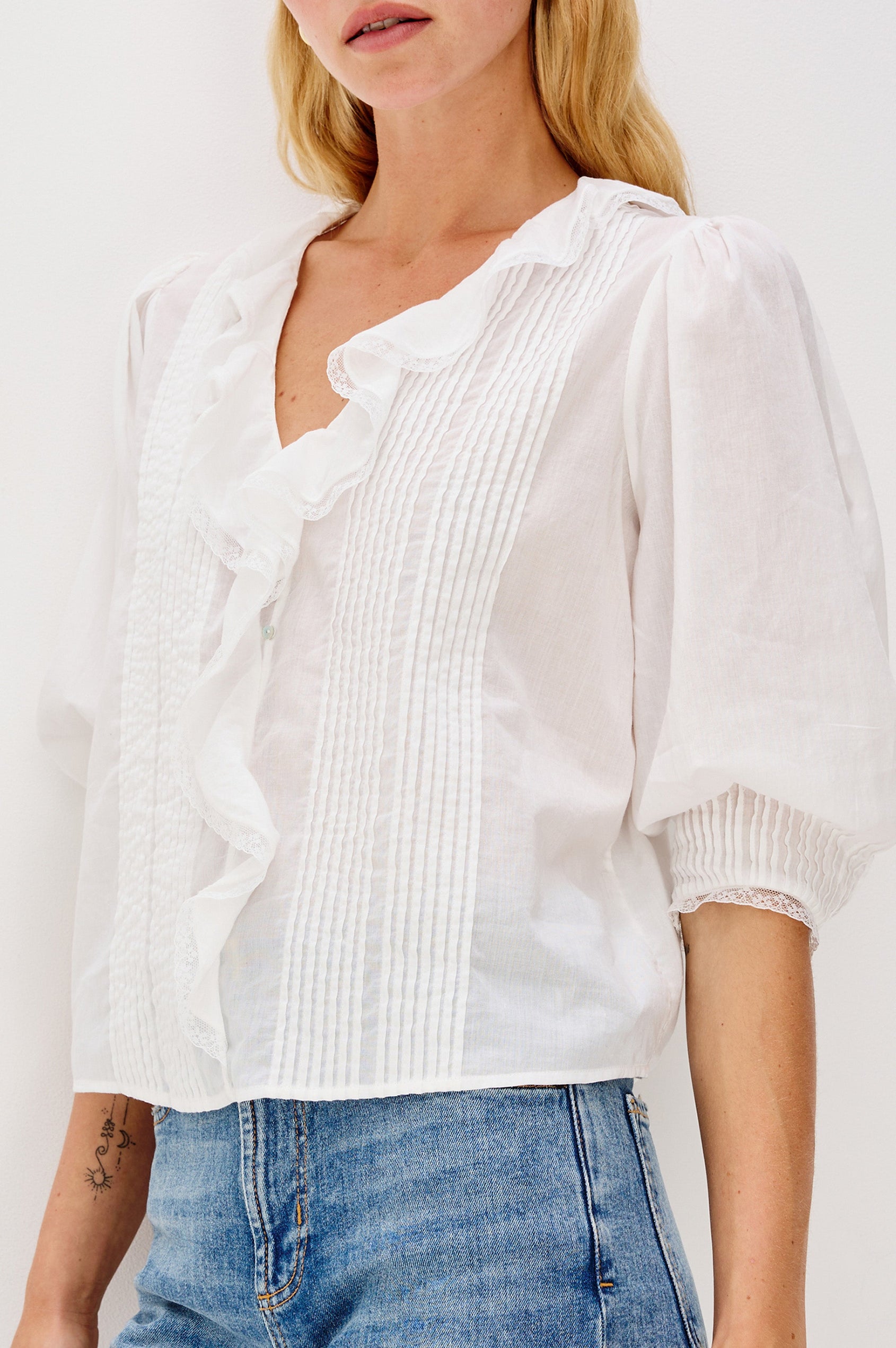 A relaxed-fit cotton blouse with cascading ruffles down the front in White Colorway. The blouse is accented with lace trim at the neckline and cuffs, adding a romantic, feminine touch. Close up of details featured on model.