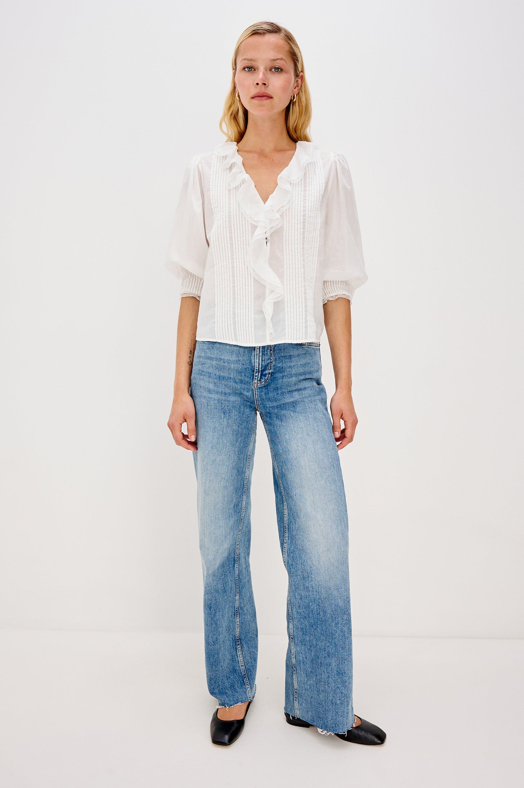 A relaxed-fit cotton blouse with cascading ruffles down the front in White Colorway. The blouse is accented with lace trim at the neckline and cuffs, adding a romantic, feminine touch. Full body front view featured on model.