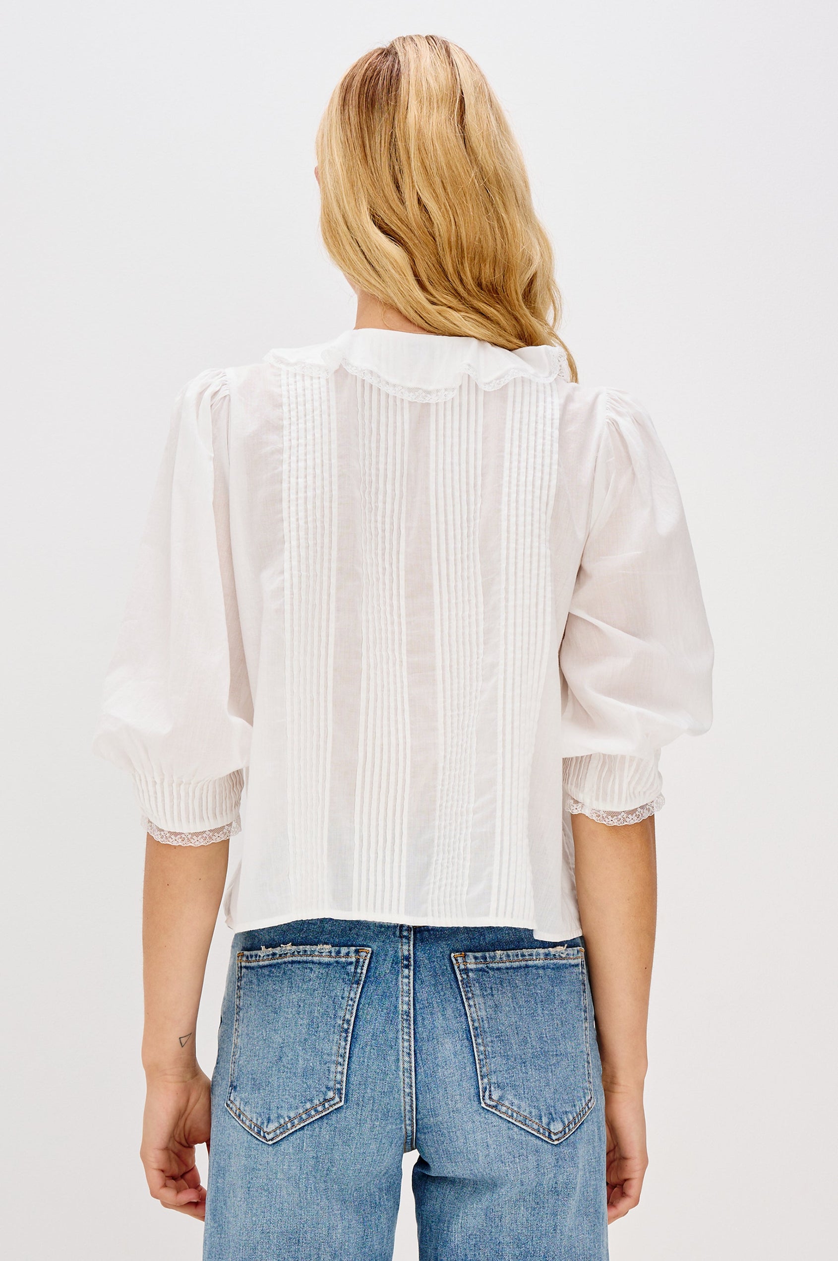 A relaxed-fit cotton blouse with cascading ruffles down the front in White Colorway. The blouse is accented with lace trim at the neckline and cuffs, adding a romantic, feminine touch. Back view featured on model.