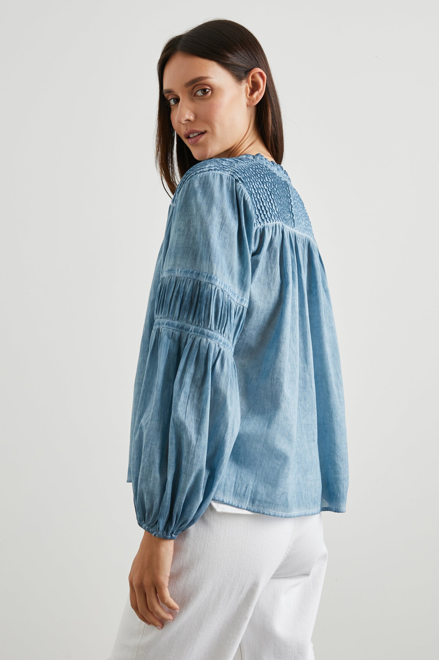 Marli Long-Sleeve Top with a V Neck, Ruffle Collar, Ruching on the Sleeves and Yoke Seam, Tiered Sleeves, and Pleats on the Yoke in Faded Blue Colorway - Side View Featured on Model 