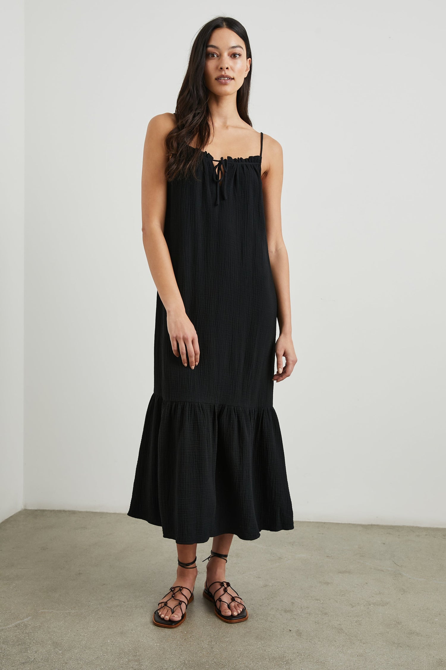 Marseille Midi Dress with Adjustable Spaghetti Straps, a Deep V Neck with a Tie, and a Lightly Ruffled Hem in Black Colorway - Front Full Body View Featured on Model