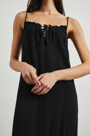 Marseille Midi Dress with Adjustable Spaghetti Straps, a Deep V Neck with a Tie, and a Lightly Ruffled Hem in Black Colorway - Front View Featured on Model