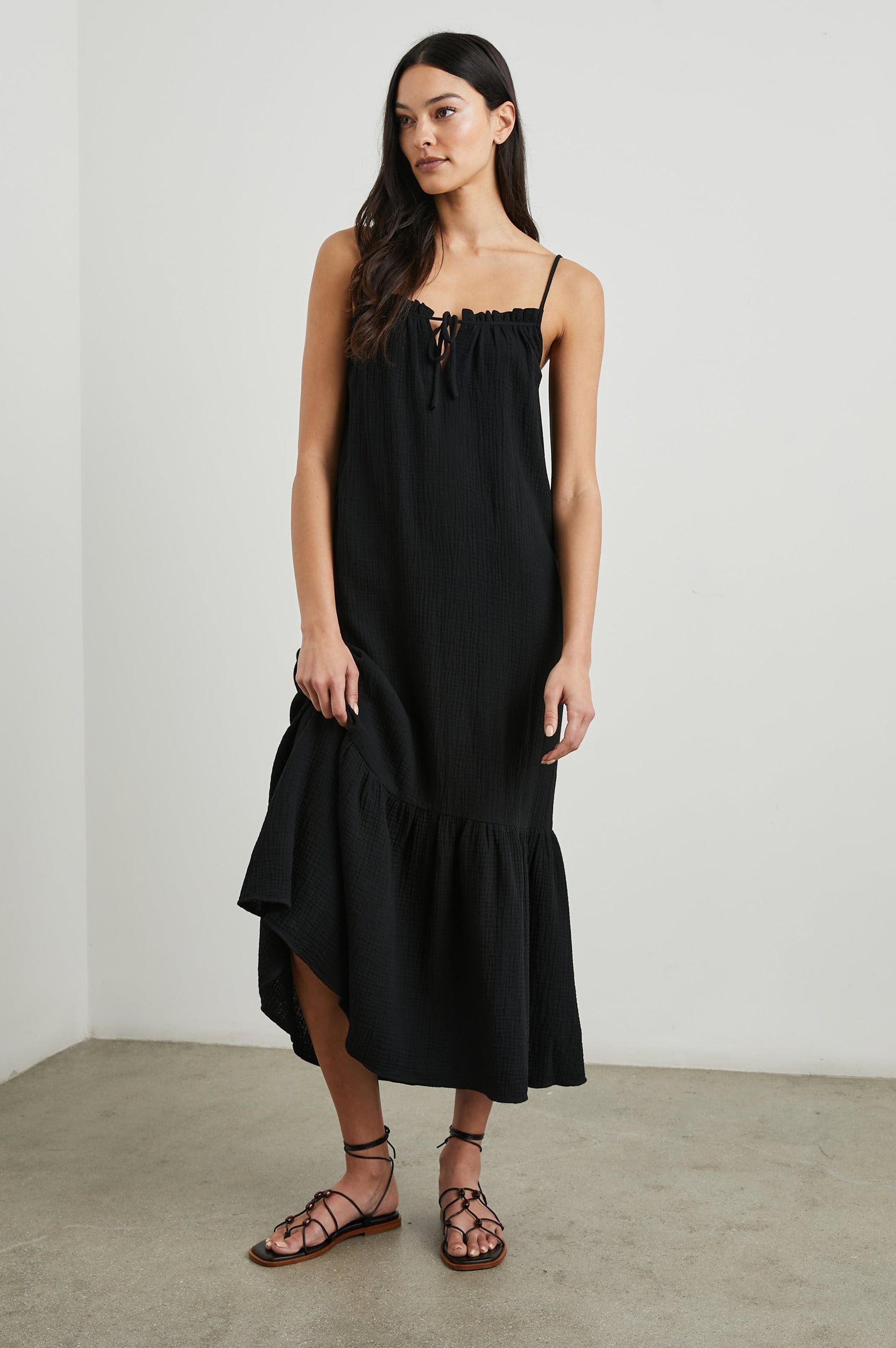 Marseille Midi Dress with Adjustable Spaghetti Straps, a Deep V Neck with a Tie, and a Lightly Ruffled Hem in Black Colorway - Front Full Body View Featured on Model
