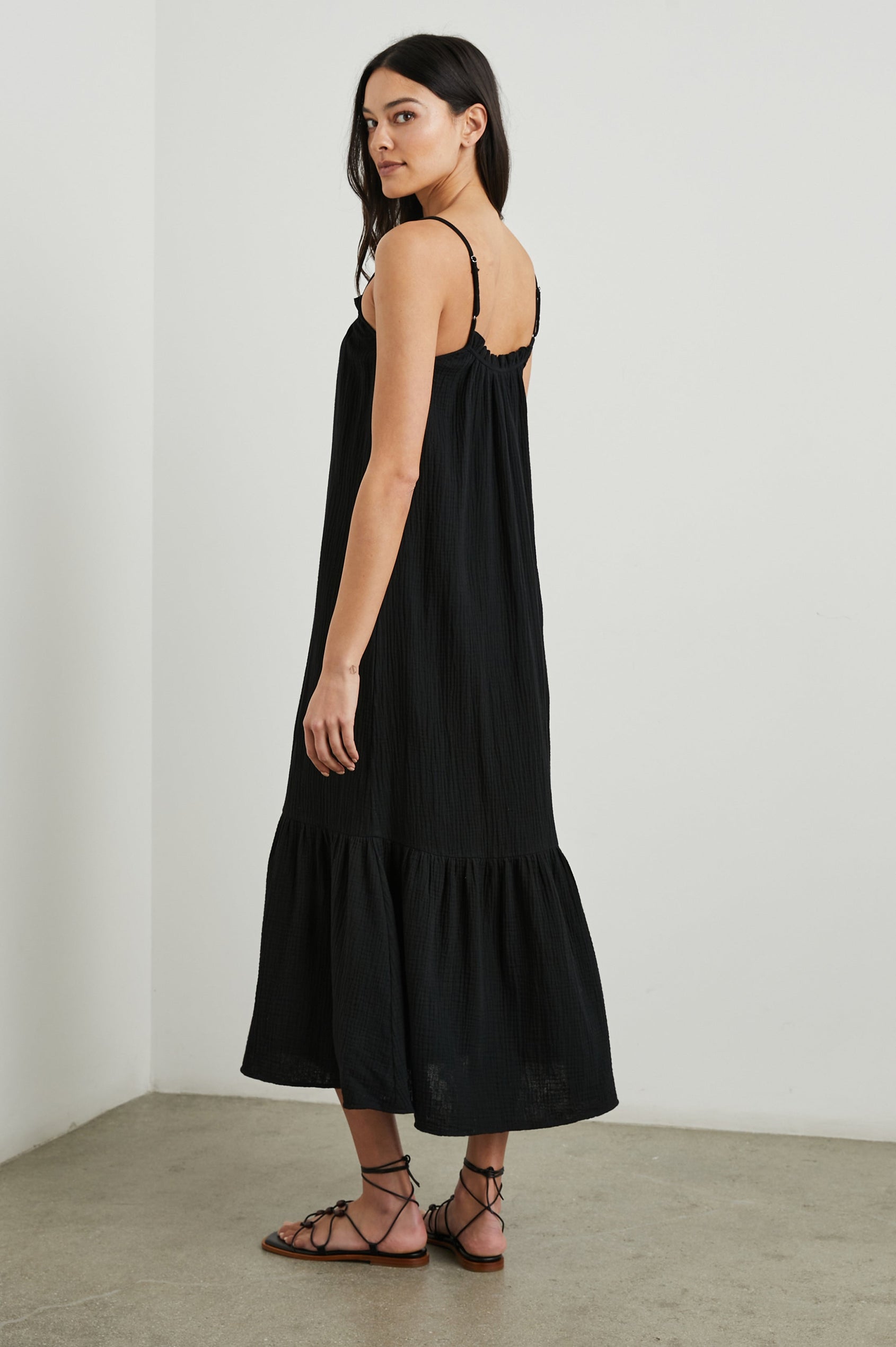 Marseille Midi Dress with Adjustable Spaghetti Straps, a Deep V Neck with a Tie, and a Lightly Ruffled Hem in Black Colorway - Side Full Body View Featured on Model