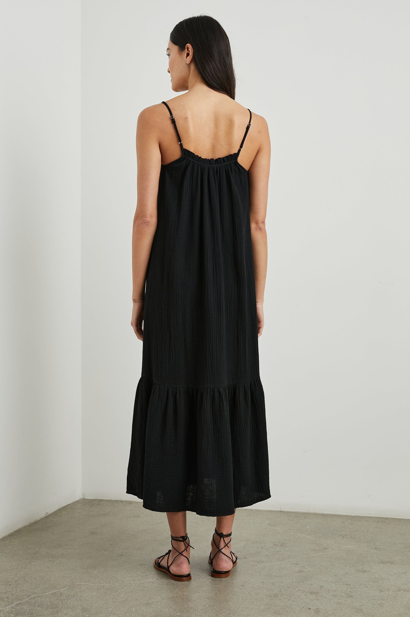 Marseille Midi Dress with Adjustable Spaghetti Straps, a Deep V Neck with a Tie, and a Lightly Ruffled Hem in Black Colorway - Back Full Body View Featured on Model