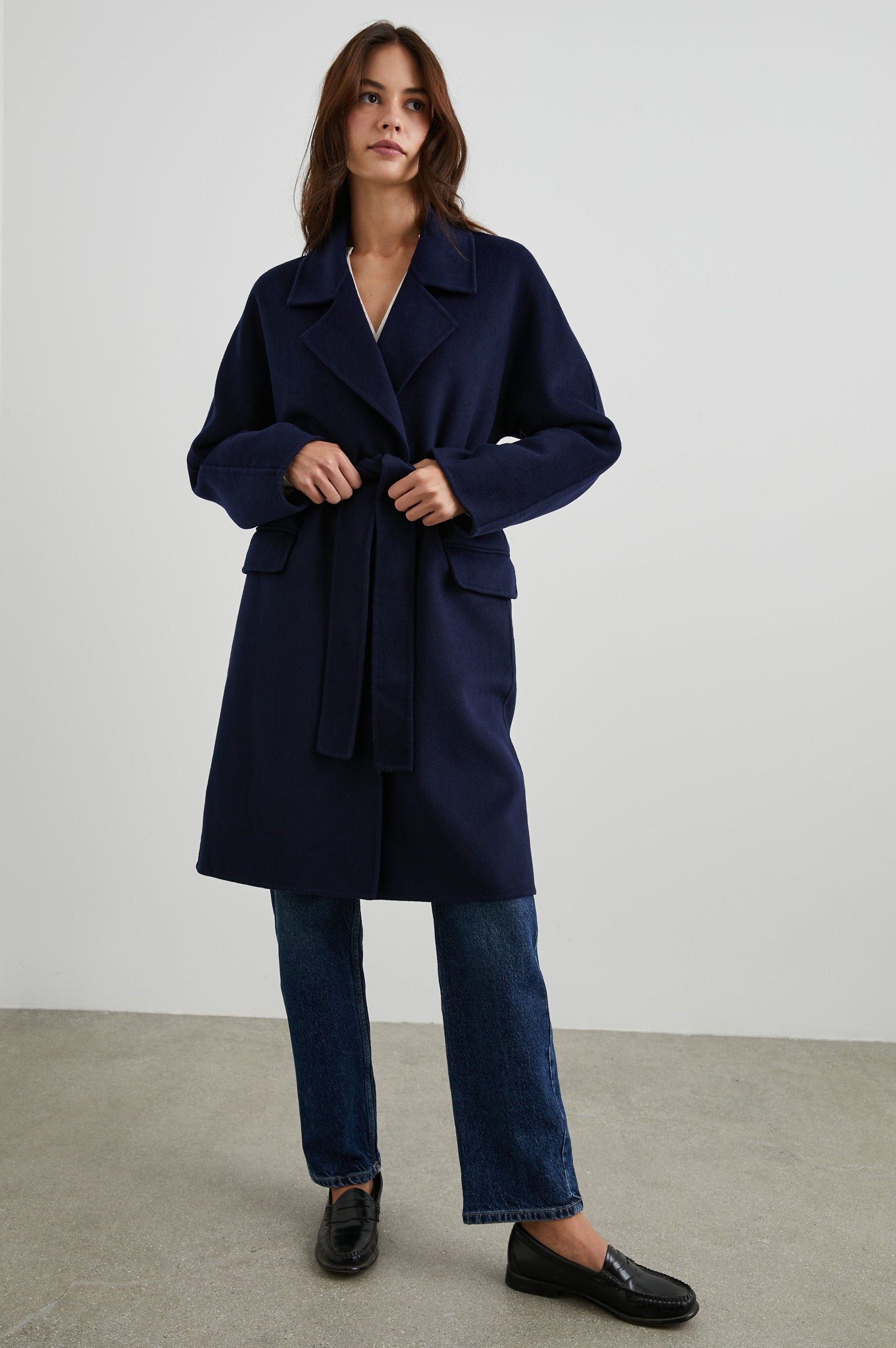 Marta Knee-Length Coat with Two Button Closure, Notched Lapels, Two Front Flap Pockets, and a Tie Belt in Navy Colorway - Front Full Body View Featured on Model 