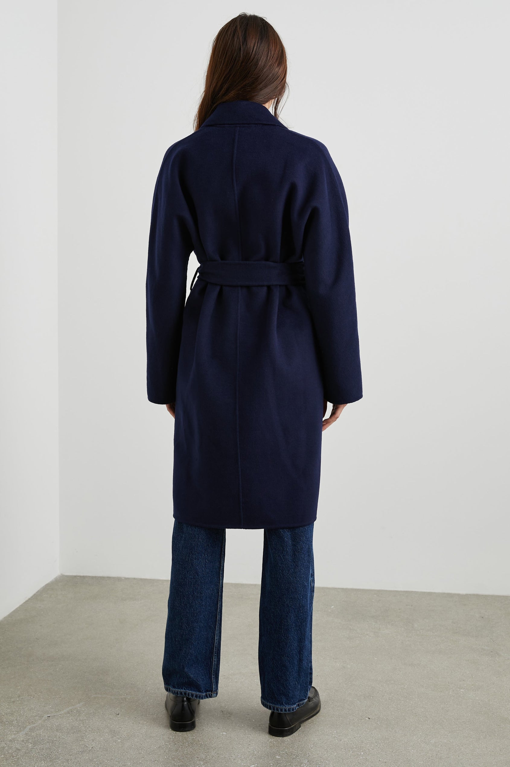 Marta Knee-Length Coat with Two Button Closure, Notched Lapels, Two Front Flap Pockets, and a Tie Belt in Navy Colorway - Back Full Body View Featured on Model 