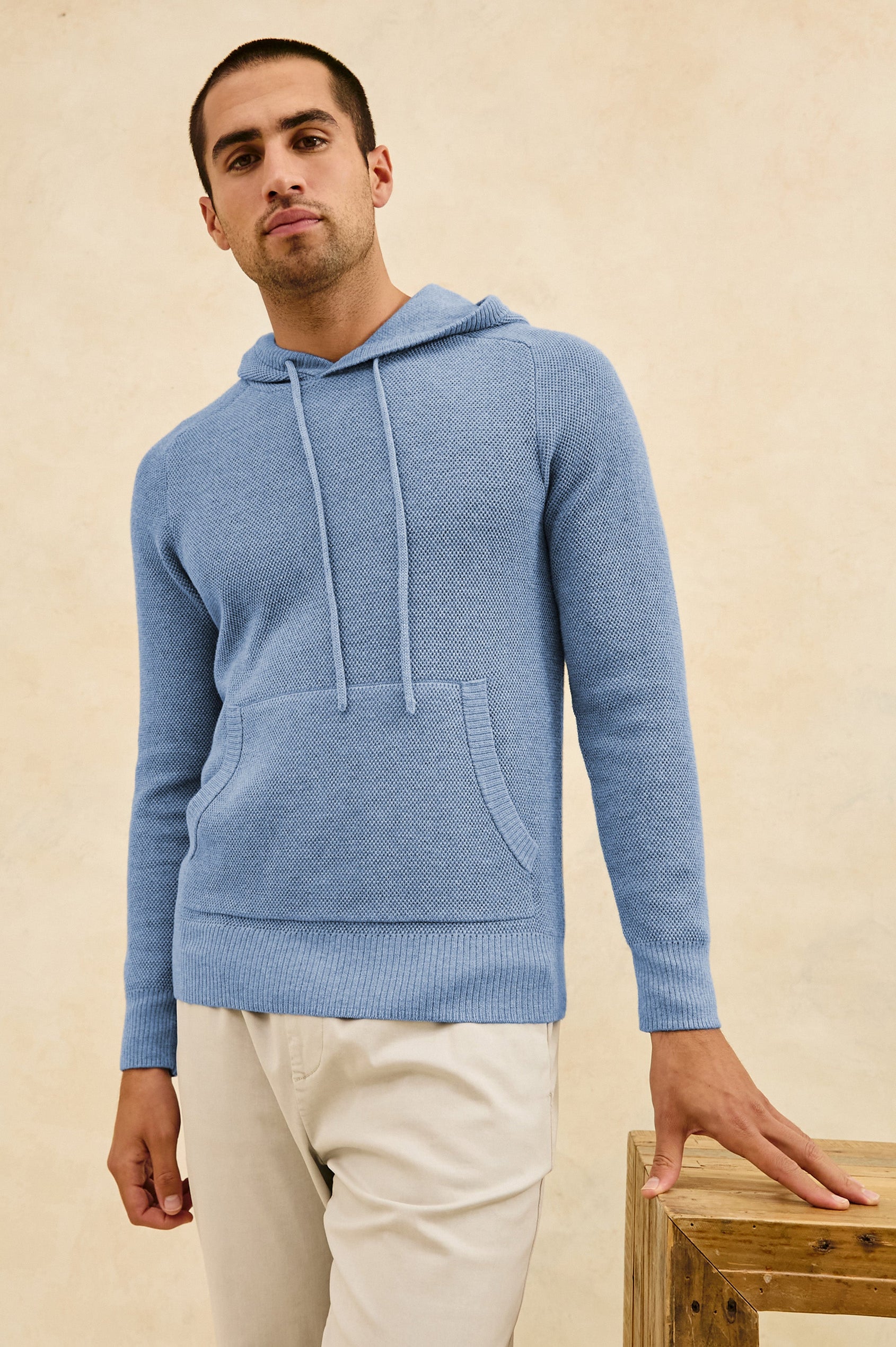 Matador knit sweater with hoodie, adjustable drawstrings, and dual side front pocket in Light Blue Heather - stylized front view on model, leaning on desk