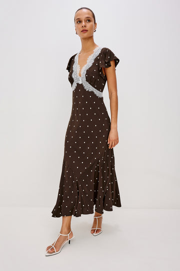 A flowing cocoa polka-dot maxi dress in crepe. The dress has a lace-trimmed V-neckline, ruffle cap sleeves, a hidden side zipper, and godet inserts that add movement to the skirt. Full Body Front View featured on Model.