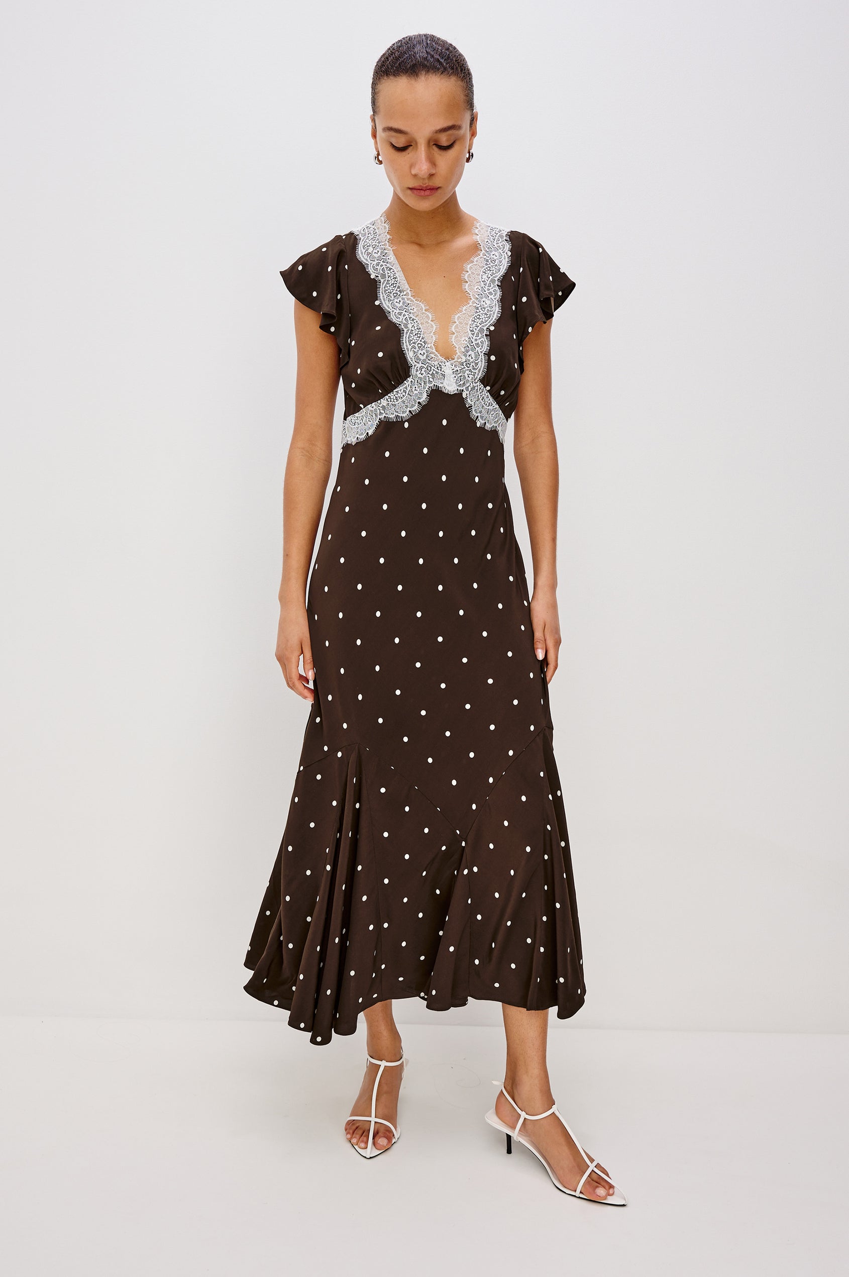 A flowing cocoa polka-dot maxi dress in crepe. The dress has a lace-trimmed V-neckline, ruffle cap sleeves, a hidden side zipper, and godet inserts that add movement to the skirt. Full Body Front View featured on Model.