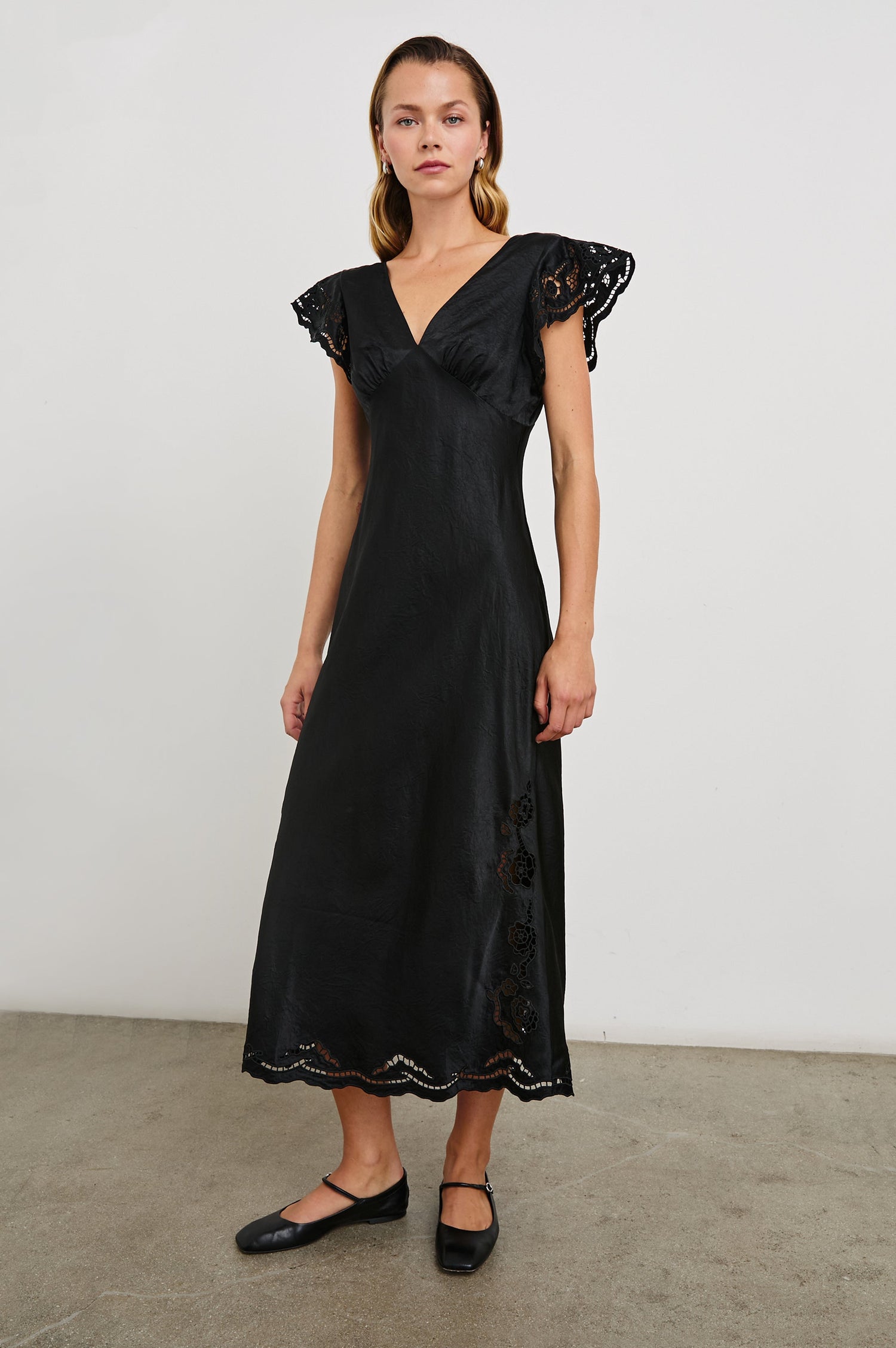 McKenna Short Sleeve Midi Dress with Flutter Sleeves, a Deep V Neck, an Eyelet Design on the Sleeves and Along the Hem and Floral Cutouts on the Skirt Sides in Black Eyelet Colorway  - Front Full Body View Featured on Model 