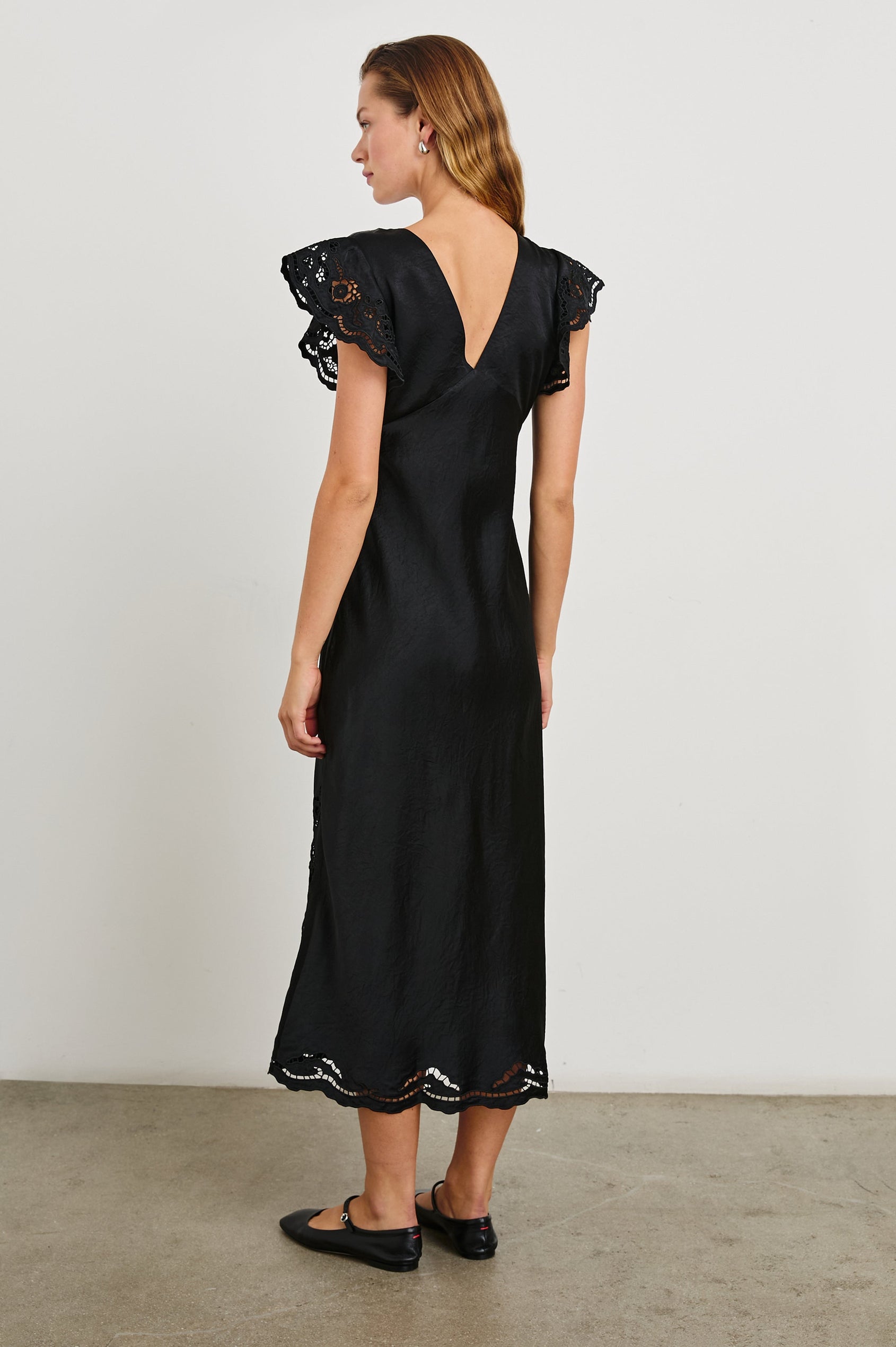 McKenna Short Sleeve Midi Dress with Flutter Sleeves, a Deep V Neck, an Eyelet Design on the Sleeves and Along the Hem and Floral Cutouts on the Skirt Sides in Black Eyelet Colorway  - Back Full Body View Featured on Model 
