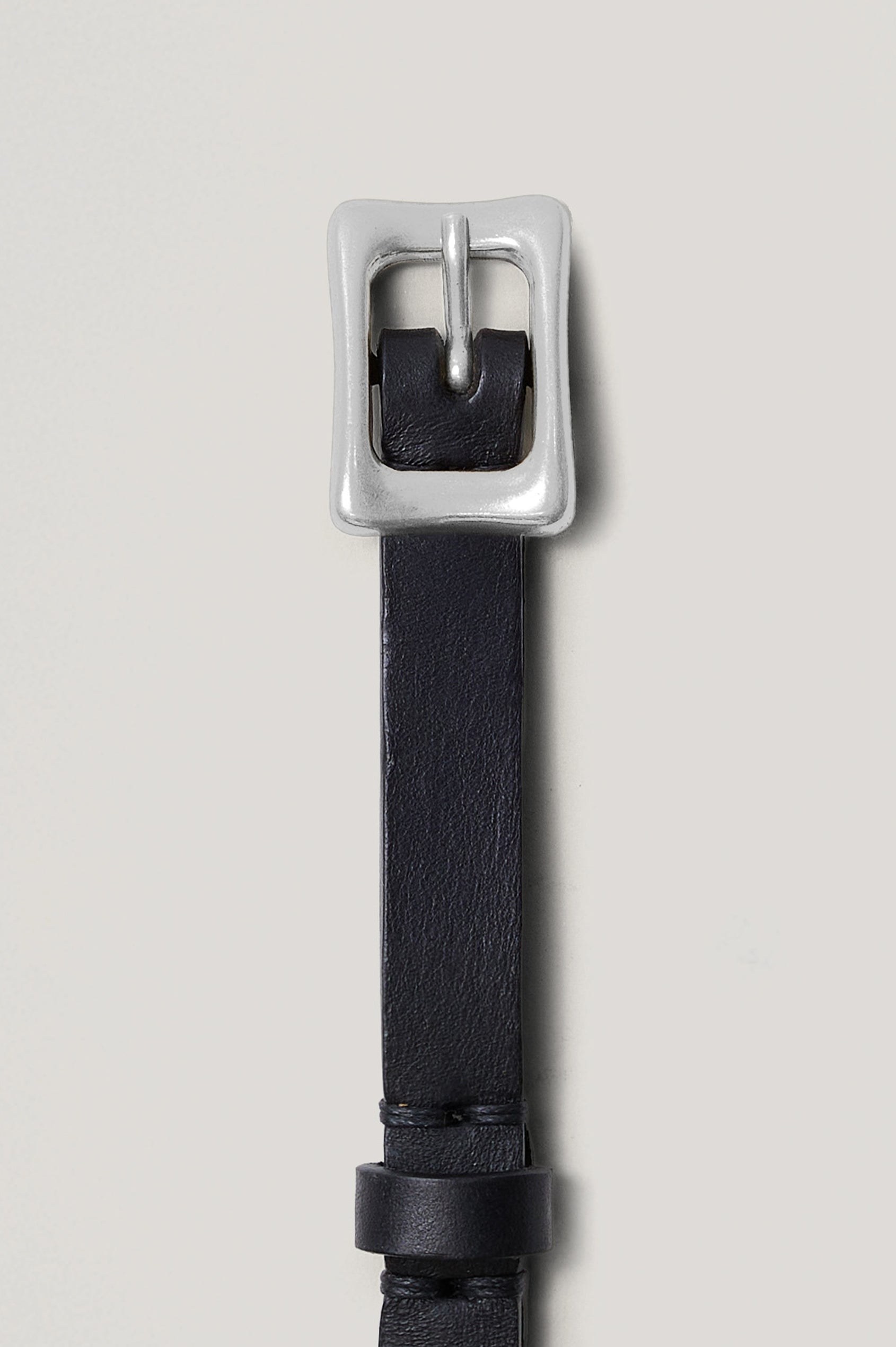 The Remi Belt in Black Leather with a polished silver buckle, unbuckled laid flat, detail shot.