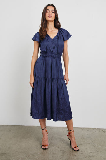 Mirielle Midi Dress with Short Flutter Sleeves, Split V-Neck with Self Tie and an A-Line Tiered Skirt in Admiral Blue Colorway. Front View Shown on Model.