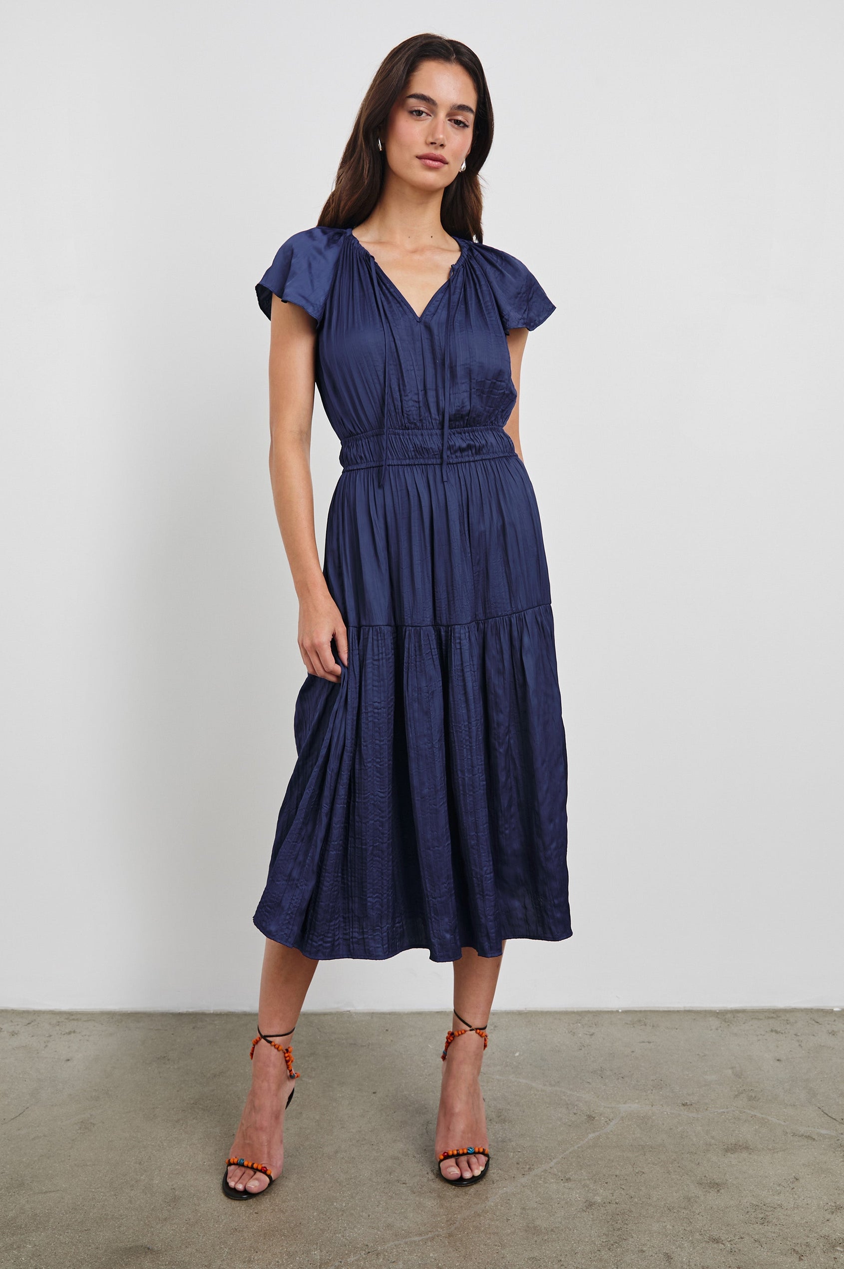 Mirielle Midi Dress with Short Flutter Sleeves, Split V-Neck with Self Tie and an A-Line Tiered Skirt in Admiral Blue Colorway. Front View Shown on Model.