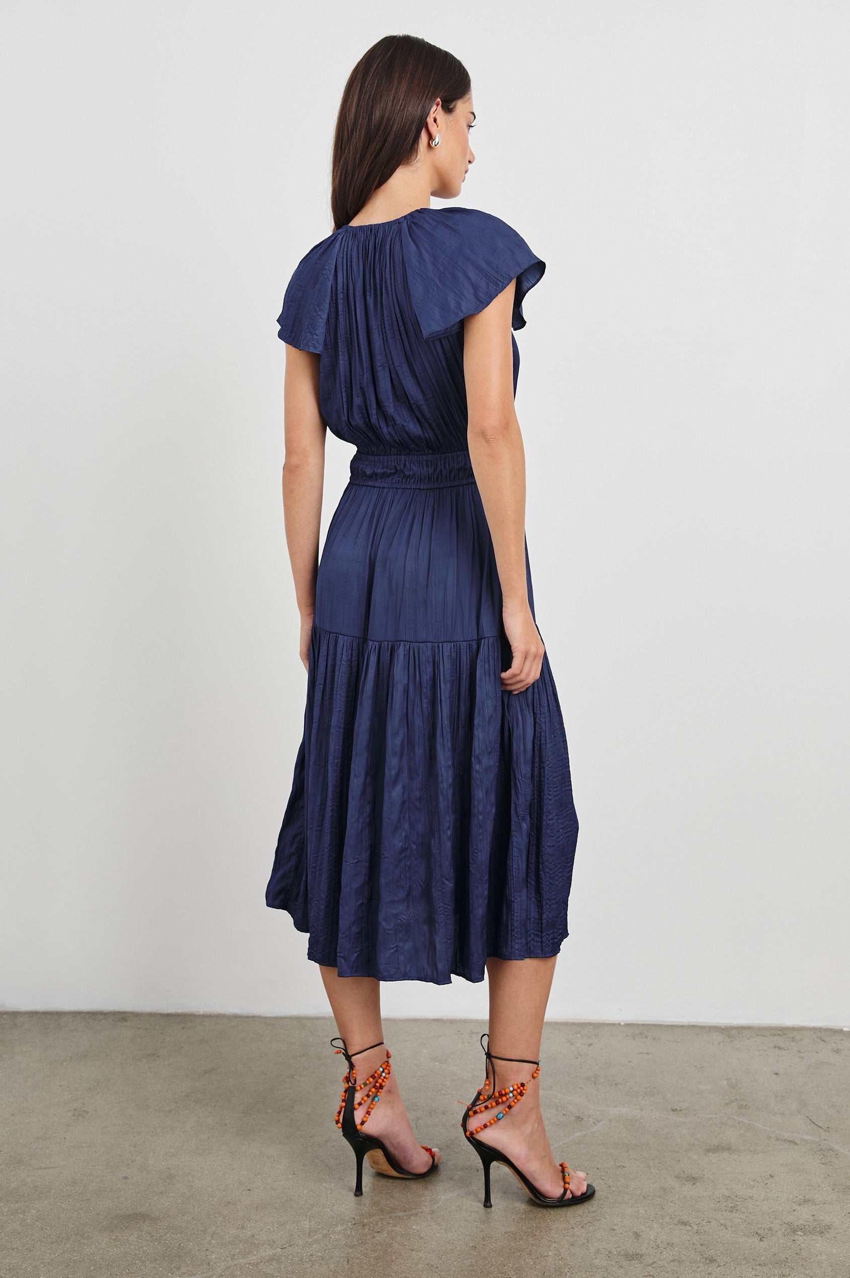 Mirielle Midi Dress with Short Flutter Sleeves, Split V-Neck with Self Tie and an A-Line Tiered Skirt in Admiral Blue Colorway. Back View Shown on Model.