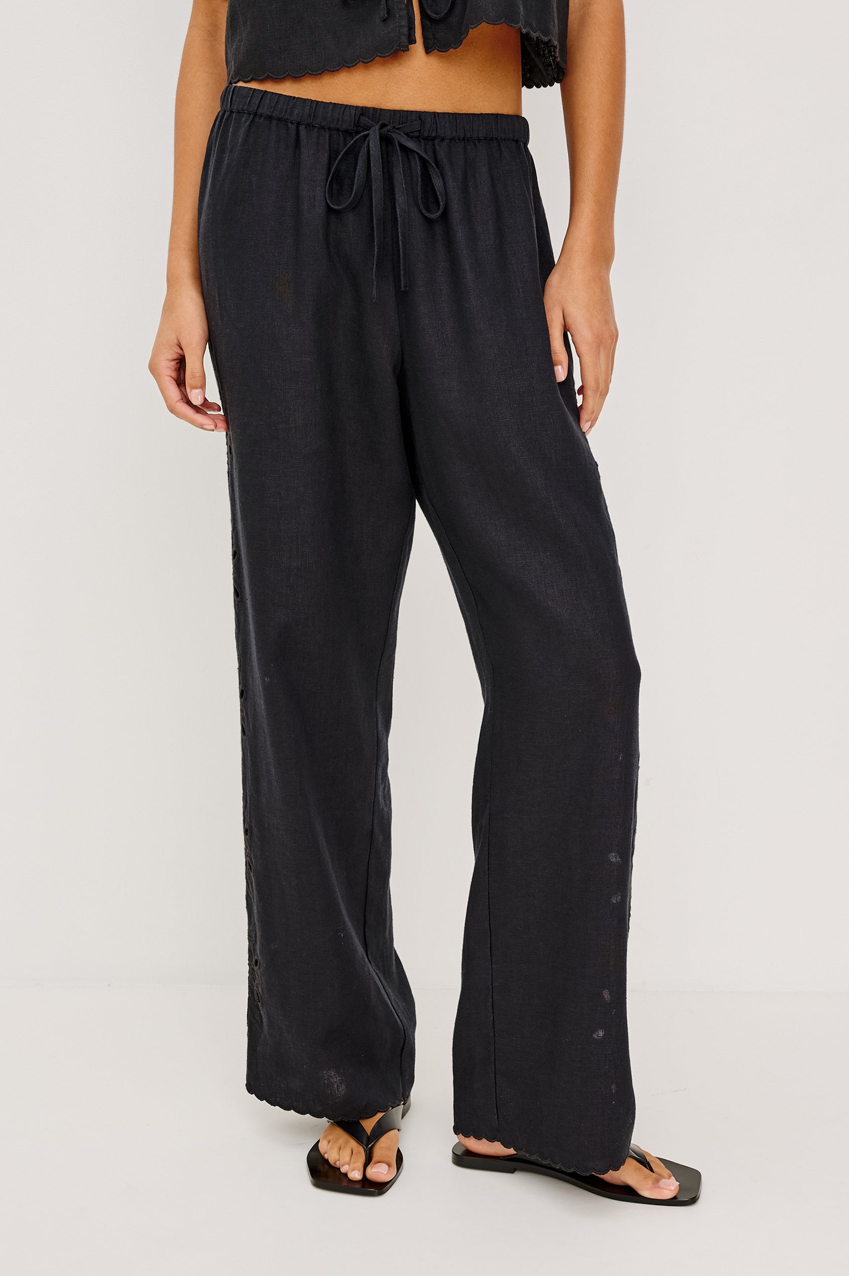 Made from midweight linen the Mirina Pant has an elastic waistband with adjustable center front ties side pockets loose straight legs and intricate floral cutwork and scalloped trim.