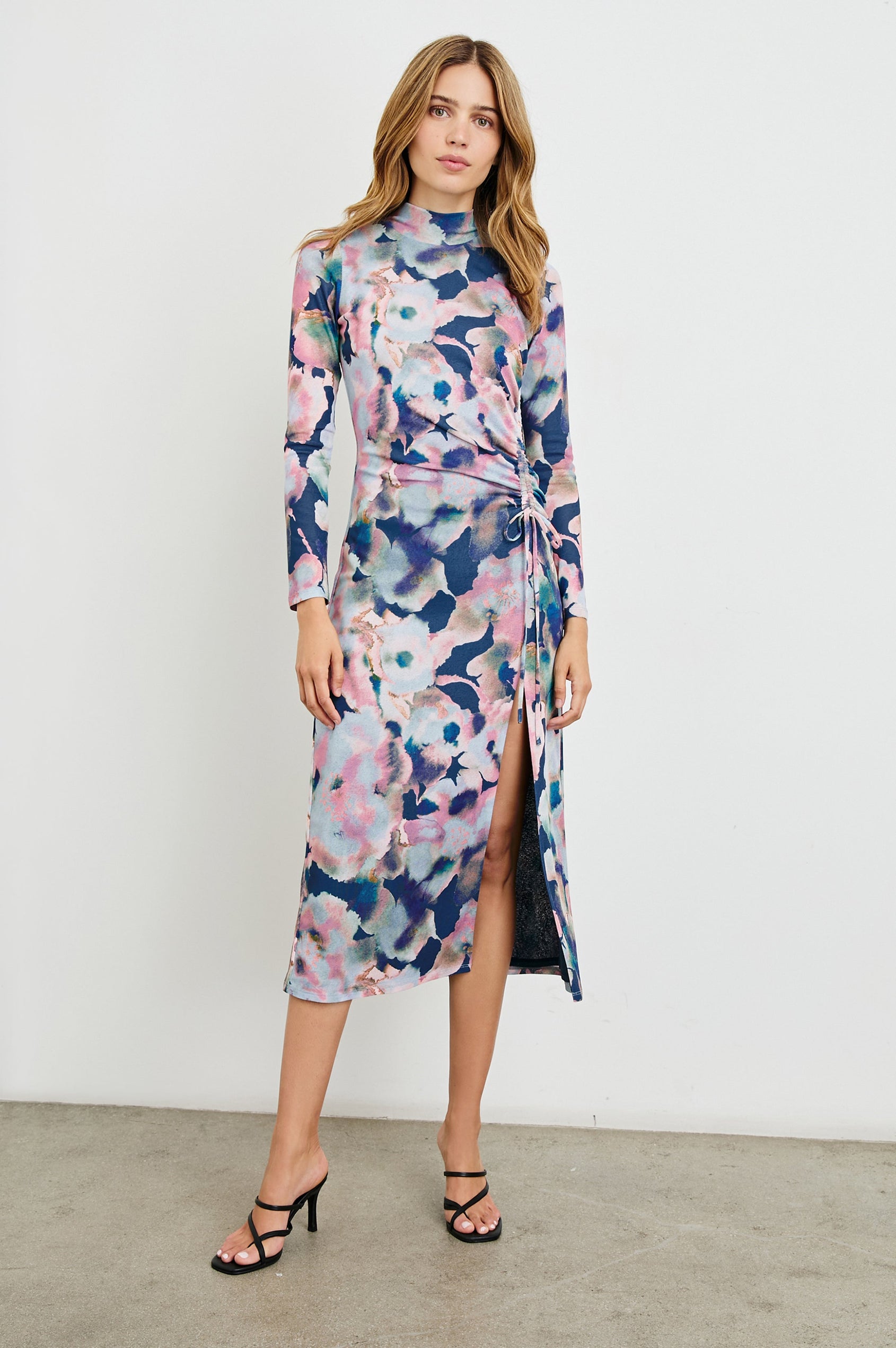 Mona Long Sleeve Midi Dress with a Mock Neck, a Side Slit and Adjustable Ruching along the Left Side with a Drawstring in Midnight Verbena Colorway, Flowers in Pinks, Browns, Greens and Blues on Midnight - Front Full Body View Featured on Model 