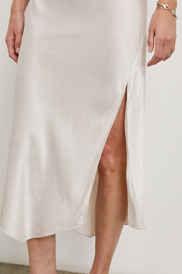 Monique Sleeveless Midi Dress with an Asymmetrical Hem Line, Side Slit, Deep V Neck, and Wide Shoulder Straps in Ivory Colorway - Front View Featured on Model