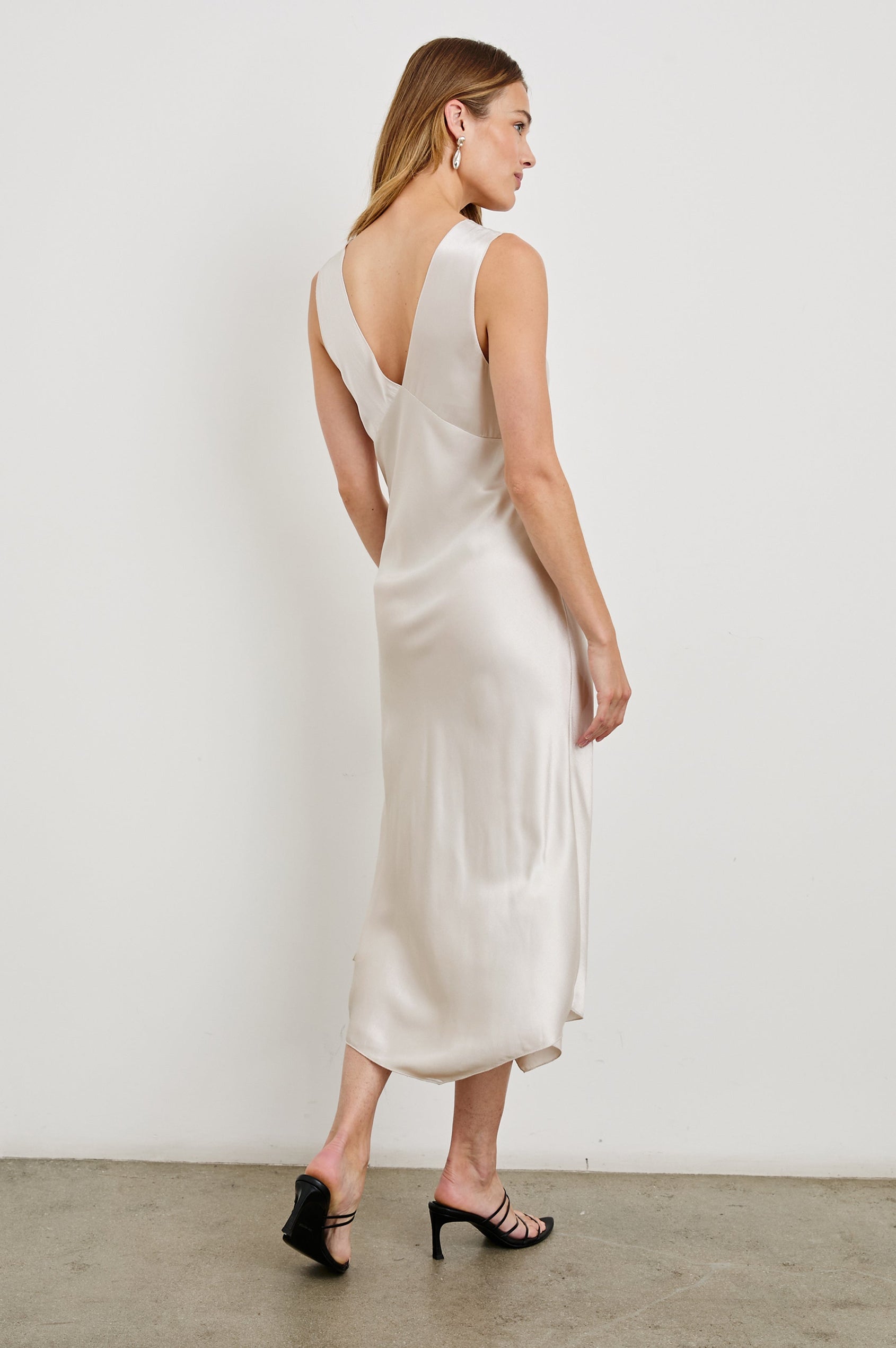 Monique Sleeveless Midi Dress with an Asymmetrical Hem Line, Side Slit, Deep V Neck, and Wide Shoulder Straps in Ivory Colorway - Back Full Body View Featured on Model