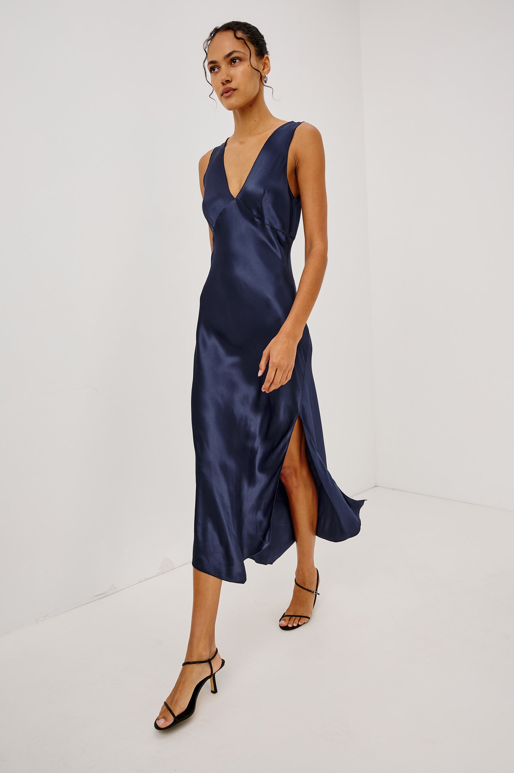Monique Midi Bias Cut Slip Dress in Satin-Back Crepe With V-Neckline, Asymmetric Hem, and Side Slit in Navy Colorway - Full Body Front View Featured on Model