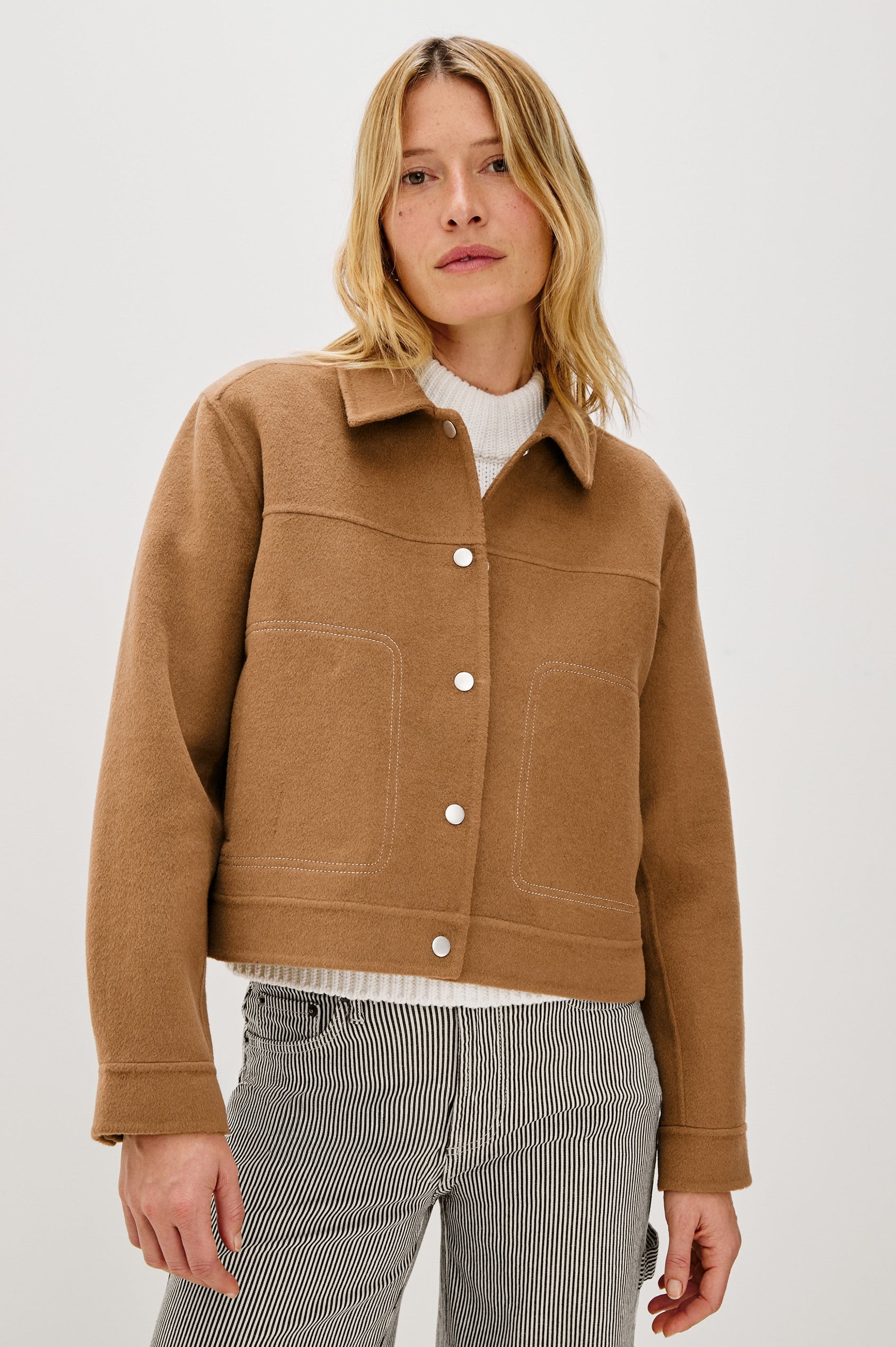 The Mountain jacket is cropped and collared with a snap front and side pockets in Camel colorway. Front view featured on model.
