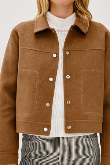 The Mountain jacket is cropped and collared with a snap front and side pockets in Camel colorway. Front detail view featured on model.