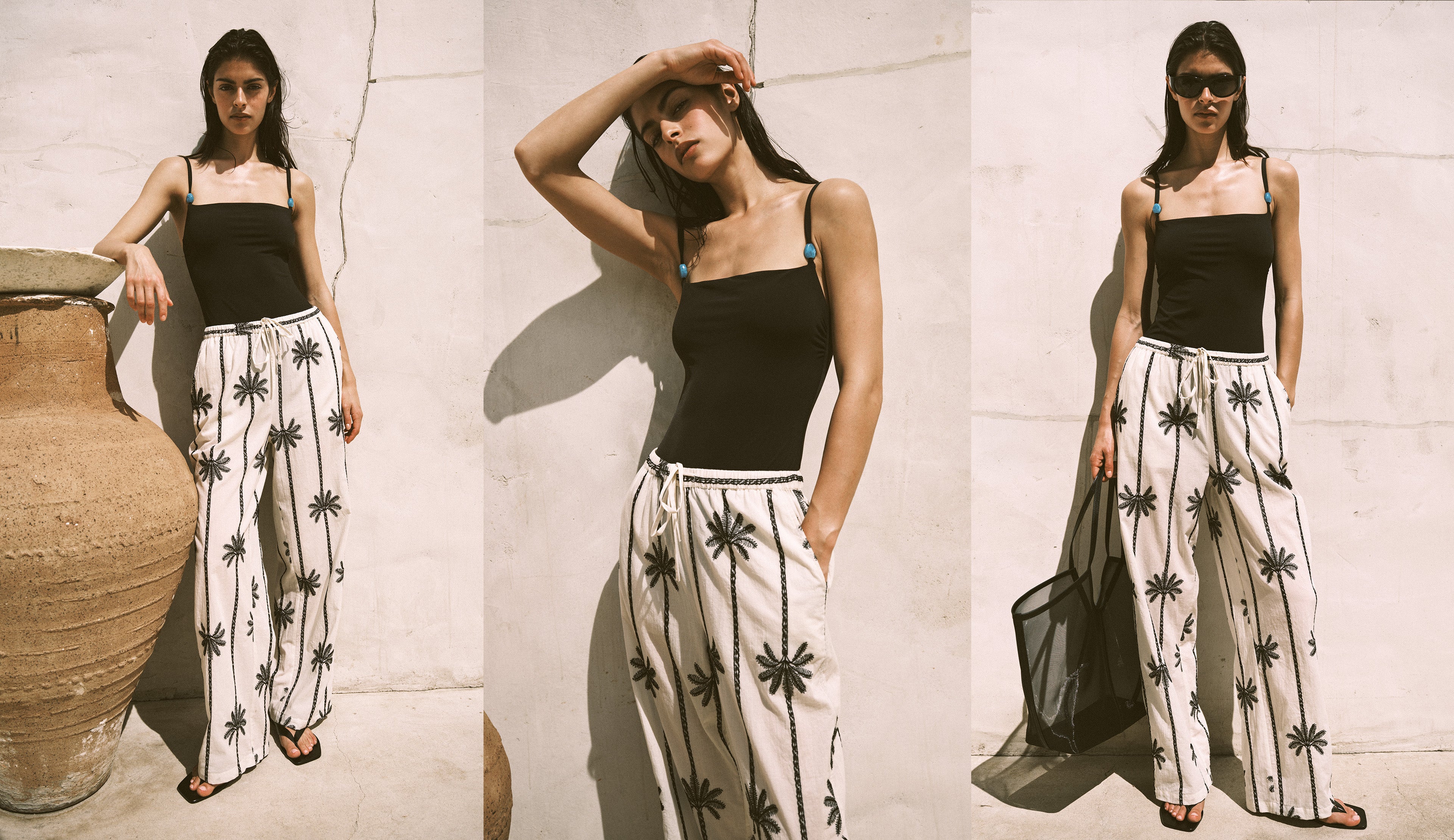 A three-panel lifestyle photo of a woman modeling a black camisole top and white wide-leg pants with a black palm tree print, posed against a light concrete wall with a large clay pot.