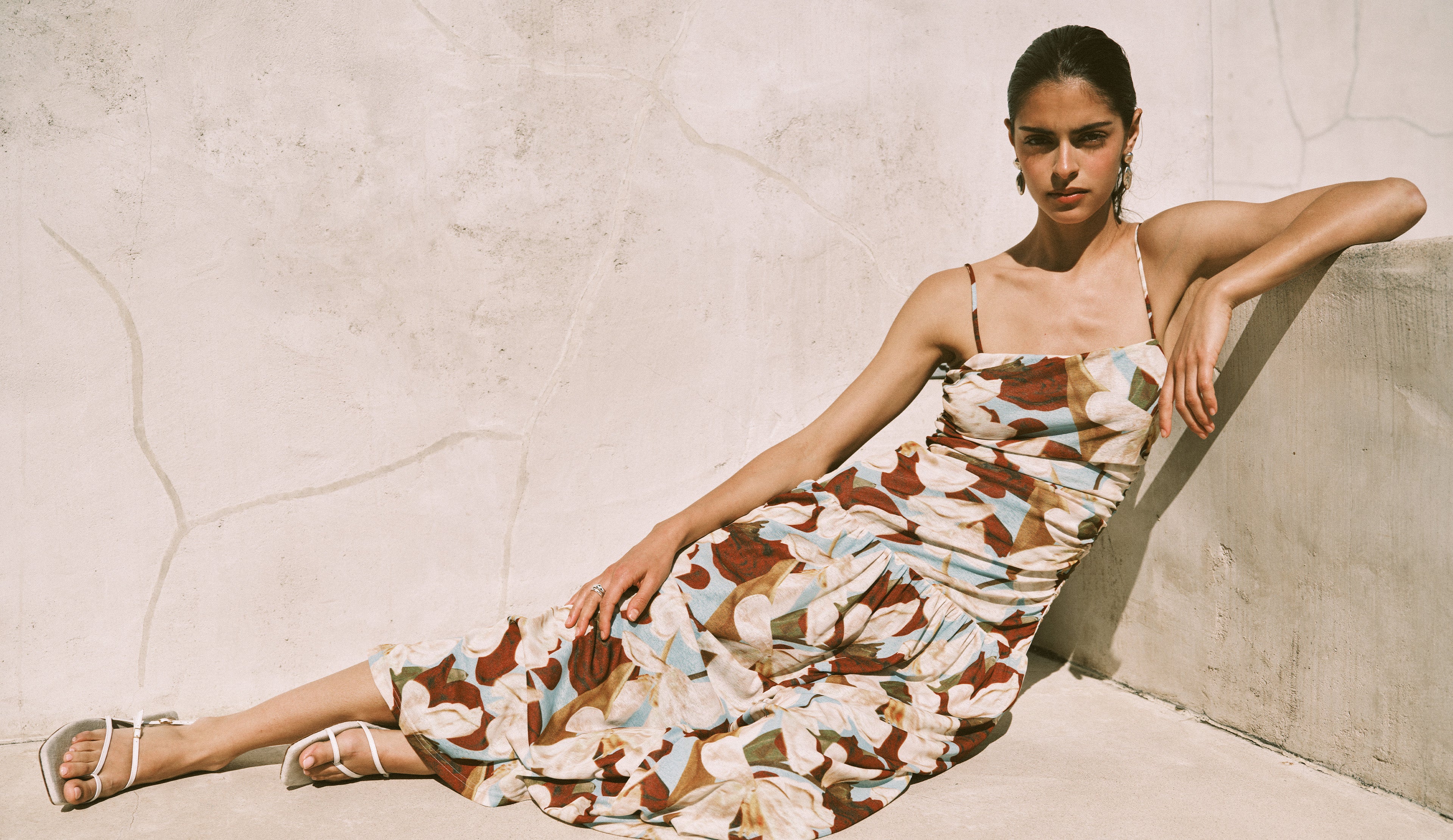 Woman in a patterned dress sitting against a textured wall.