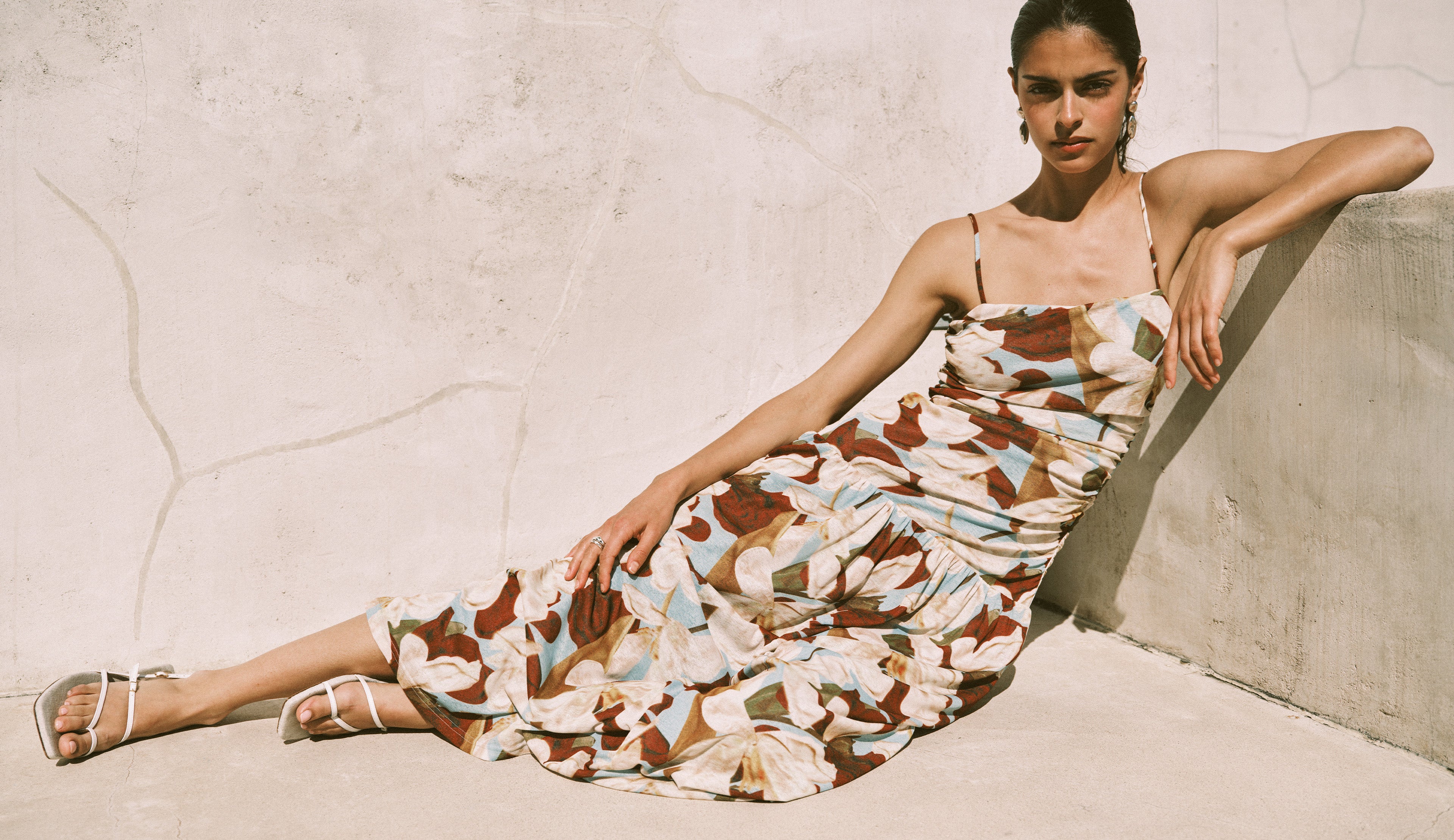 Woman wearing a colorful neutral maxi dress while leaning against a wall