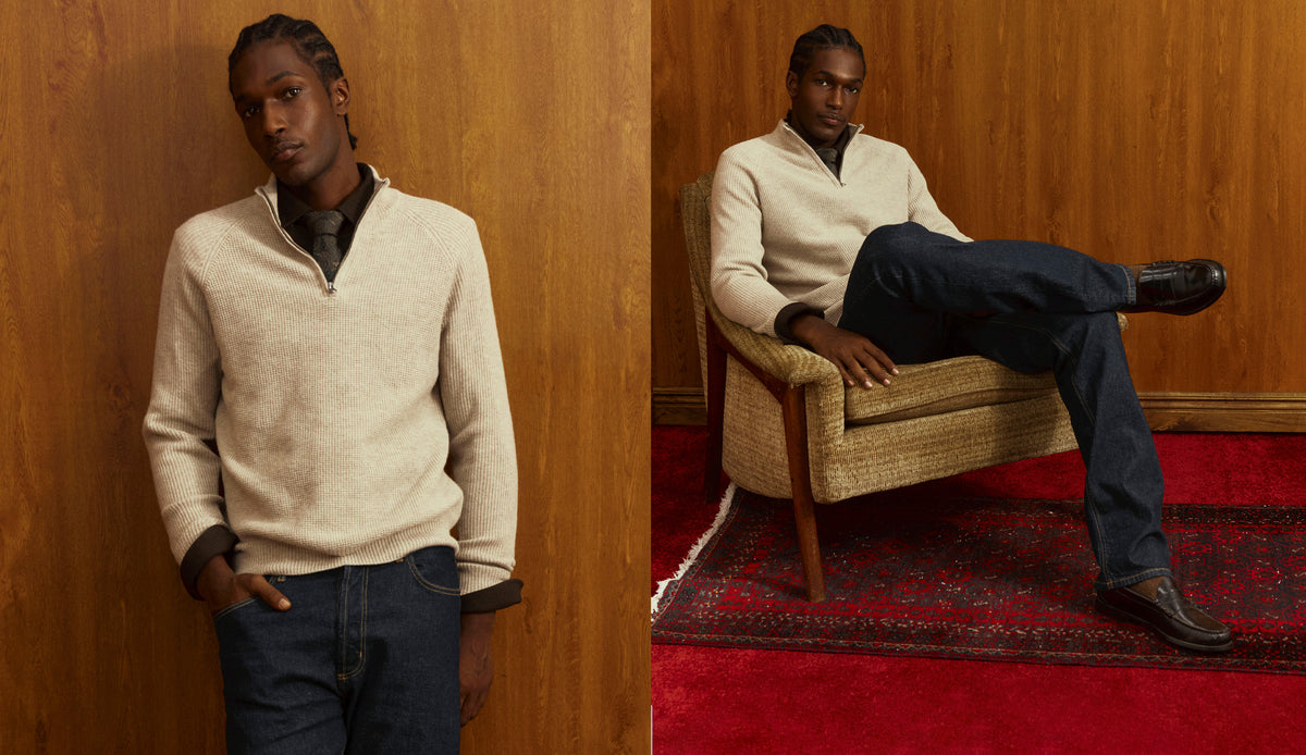 A split-screen lifestyle photo of a male model wearing a cream-colored quarter-zip sweater and dark blue jeans, posed against a wood-paneled wall and sitting in a woven armchair on a red patterned rug.