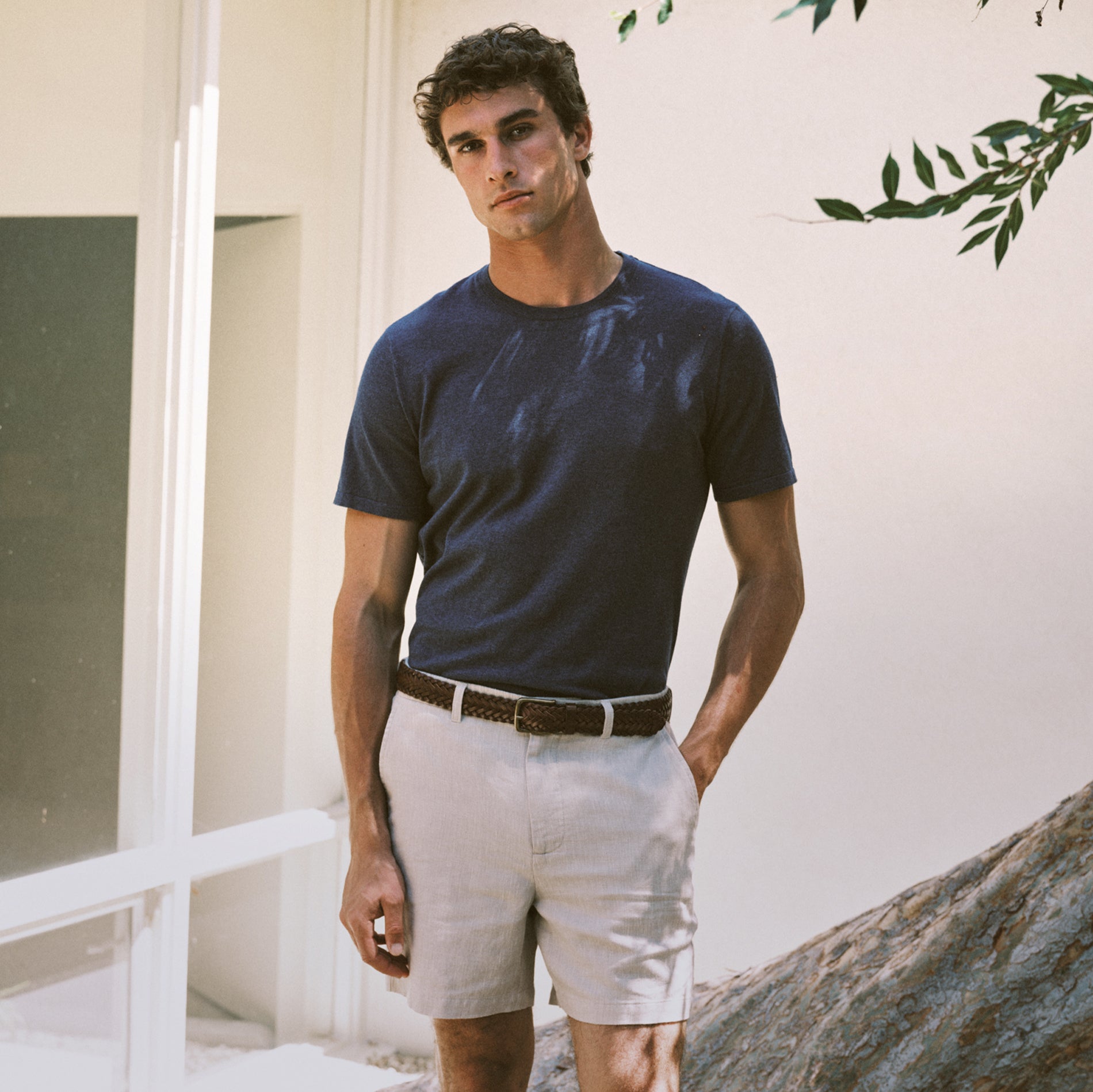 Man wearing a navy blue t-shirt and light-colored shorts standing outdoors.