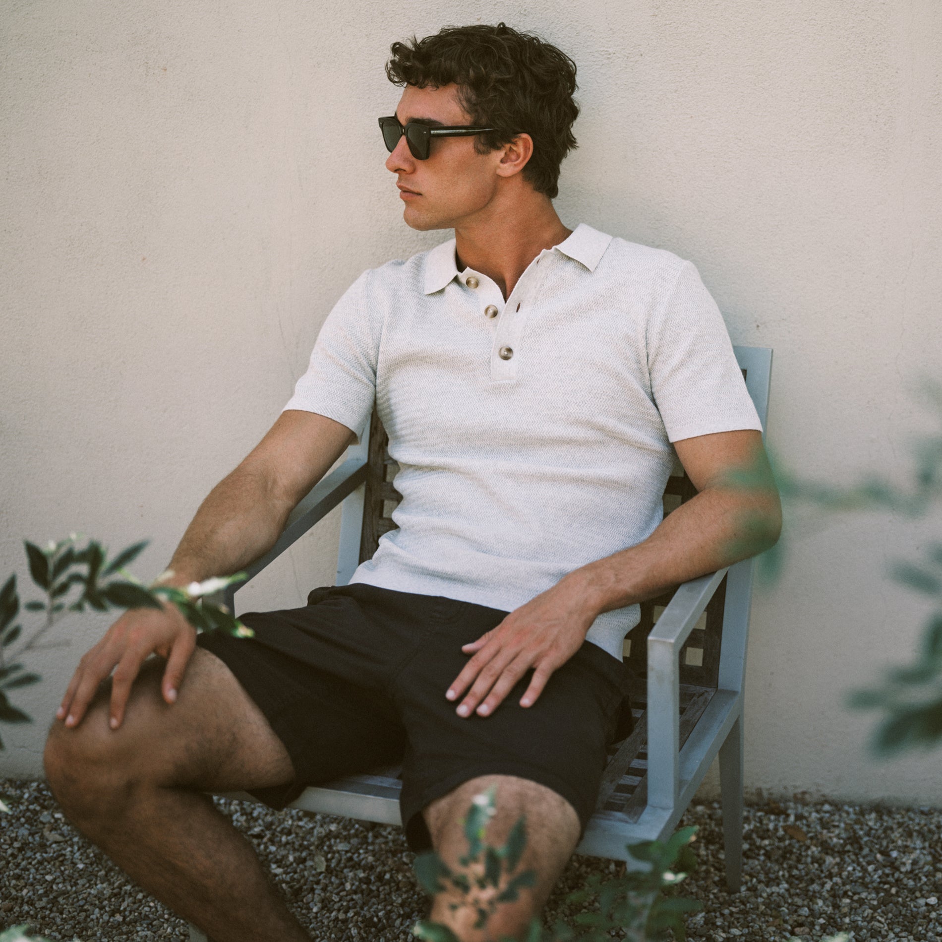 Man wearing a white polo and black shorts sitting on a chair