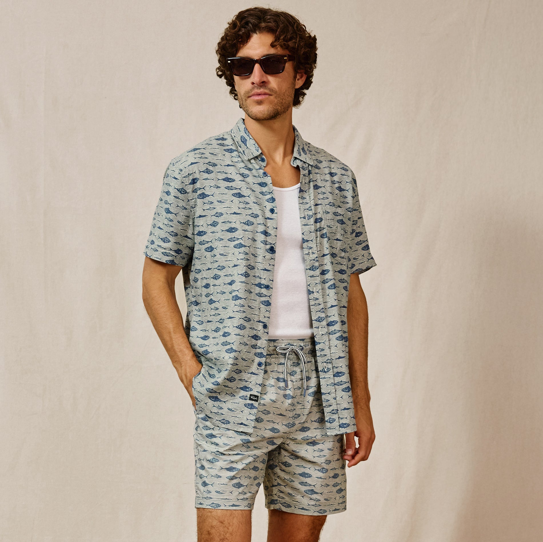 Man wearing a patterned shirt and shorts set with sunglasses on a beige background