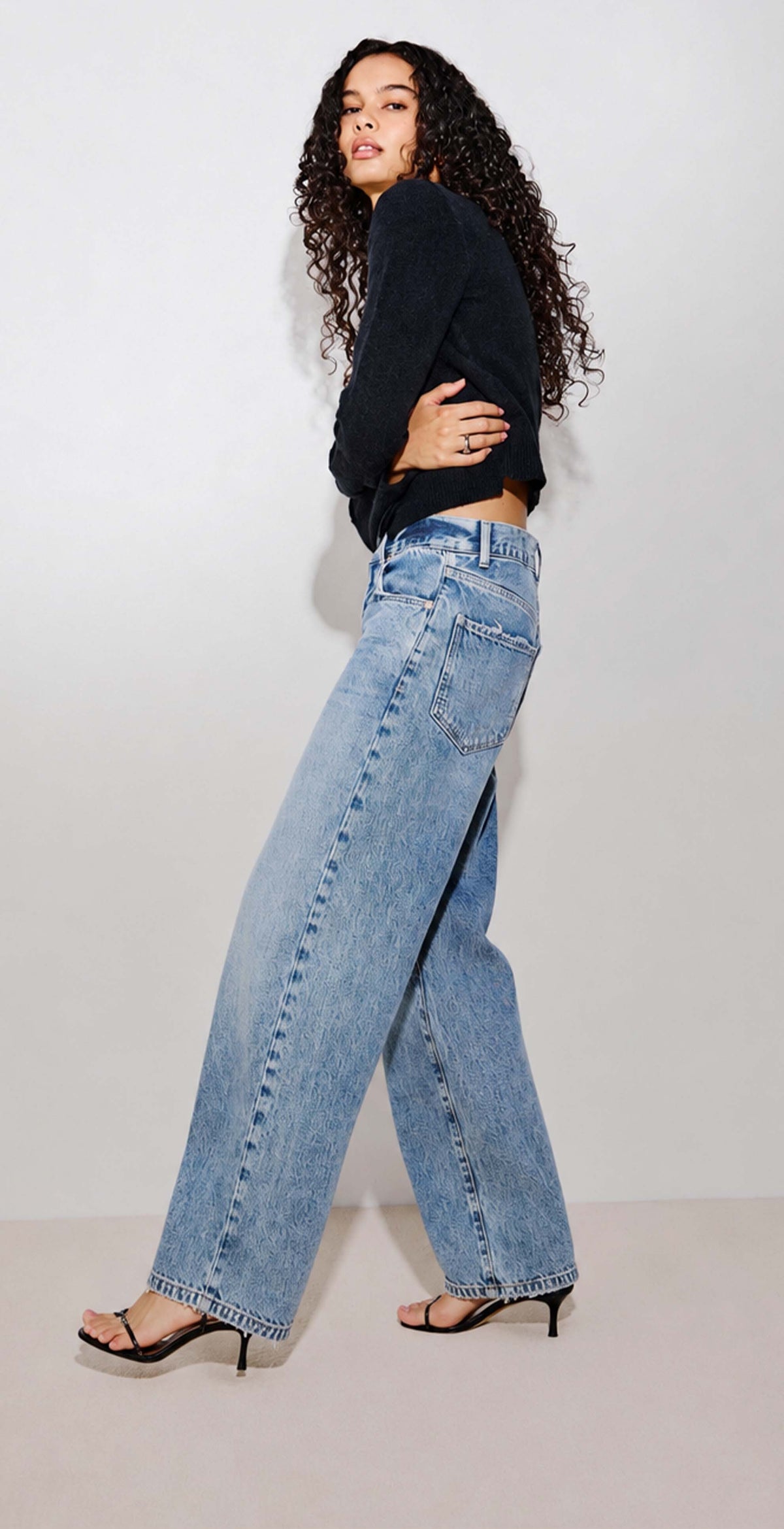 Three-panel collage showing a model wearing light-wash wide-leg blue jeans with a black long-sleeve top. The left panel shows a full-body front view, the center panel shows a close-up back view of the jeans, and the right panel shows a side/back view.