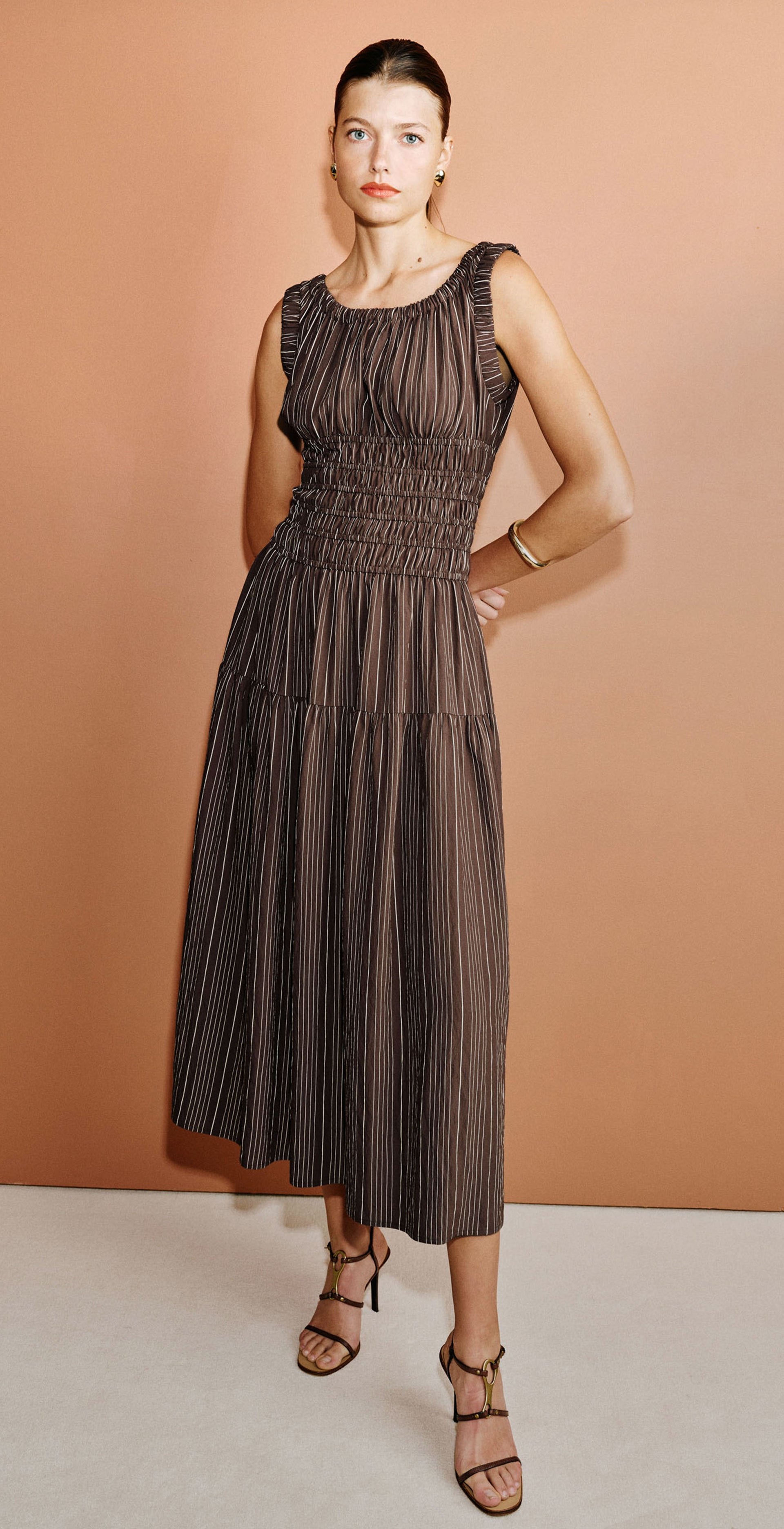 Woman wearing a brown striped midi dress with heels against an orange background.