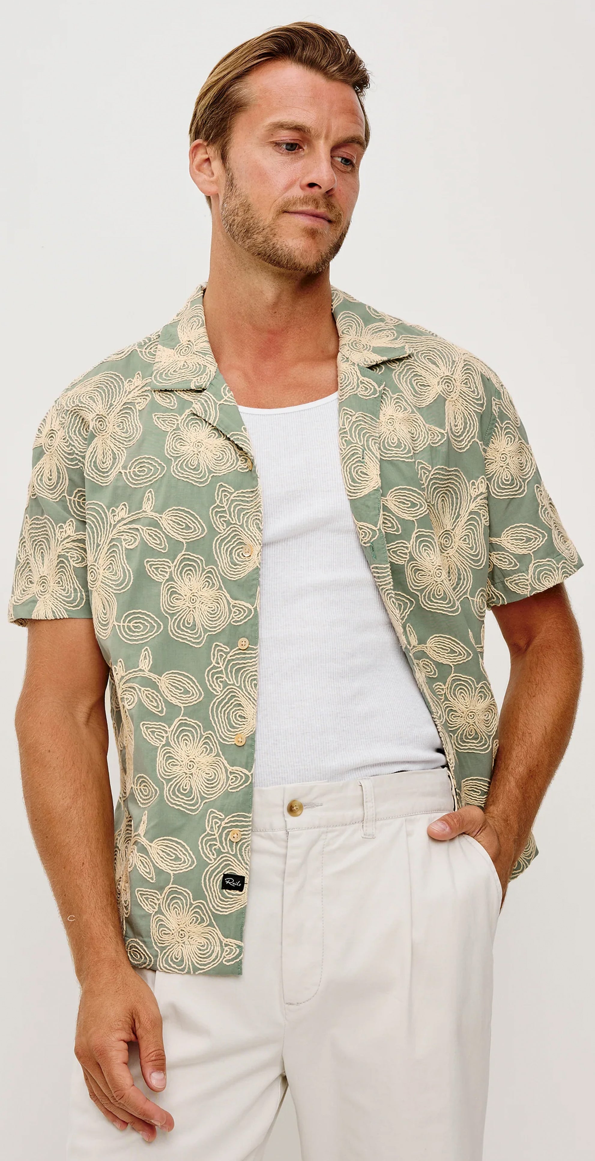 Man wearing a patterned shirt and white pants on a plain background