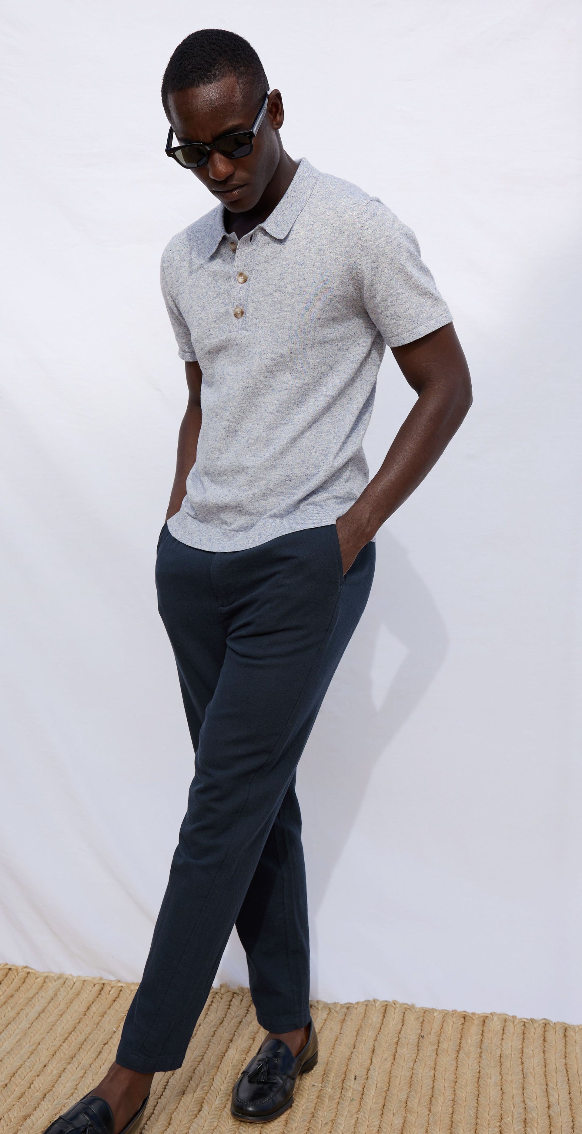 Man wearing a light gray polo shirt and dark pants against a white background