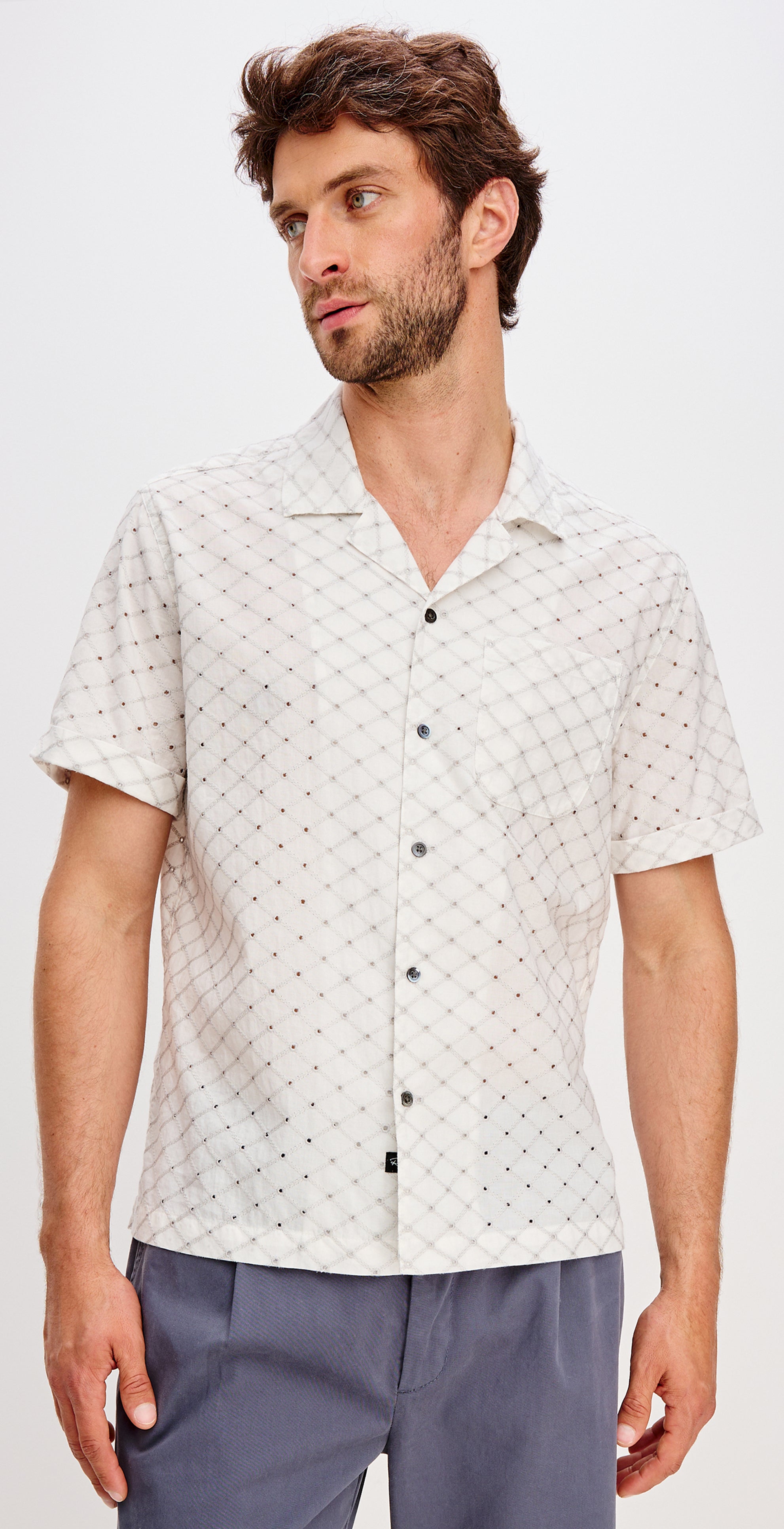 Man wearing a patterned white shirt with a plain background.