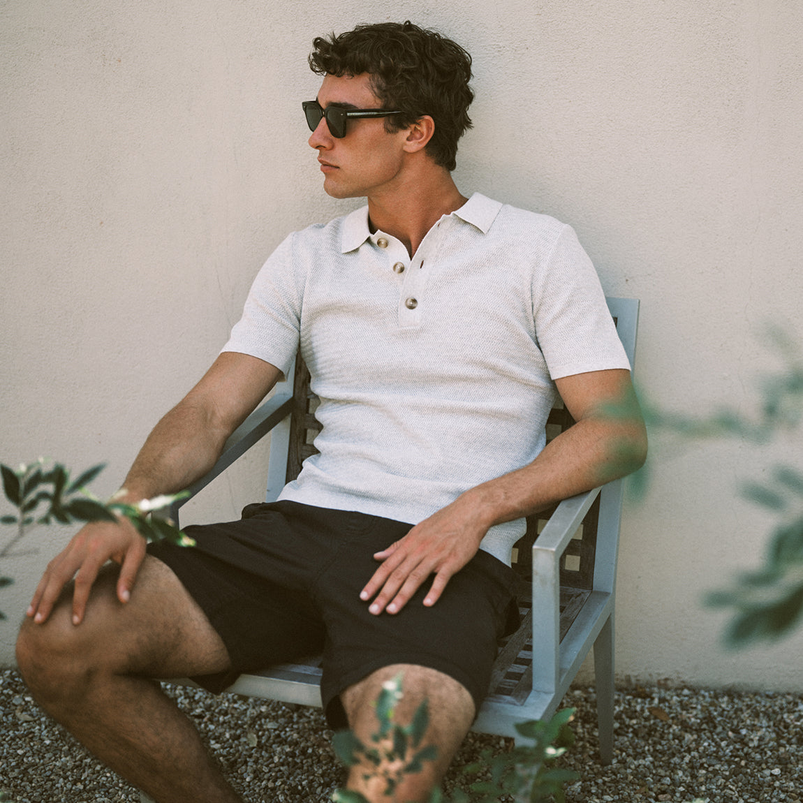 Man wearing a white polo and black shorts sitting on a chair