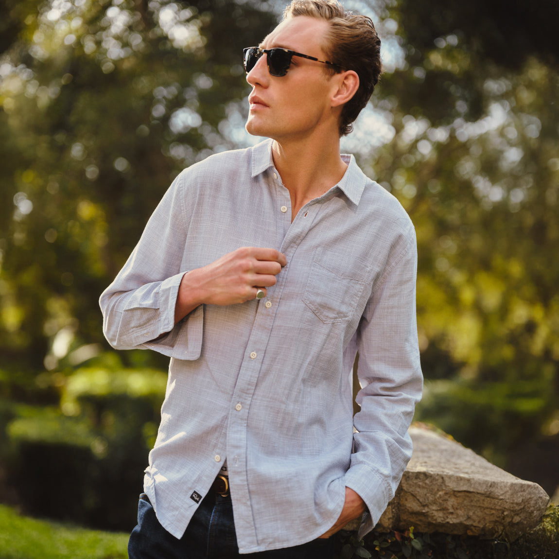 Man wearing a blue button-down shirt with sunglasses and dark pants