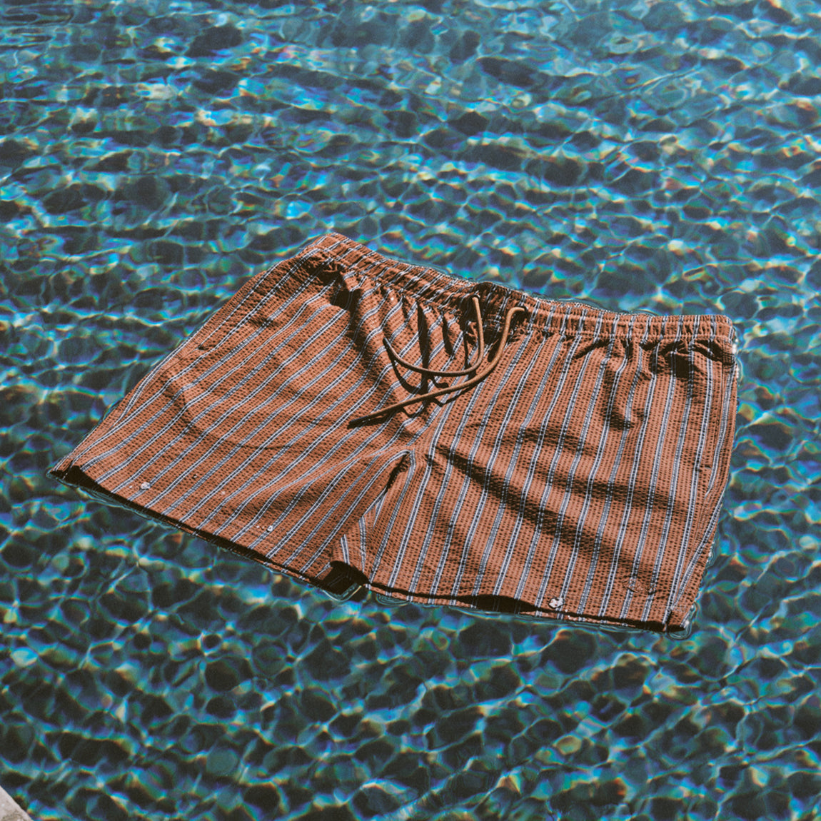 Brown striped swim shorts floating on a pool surface