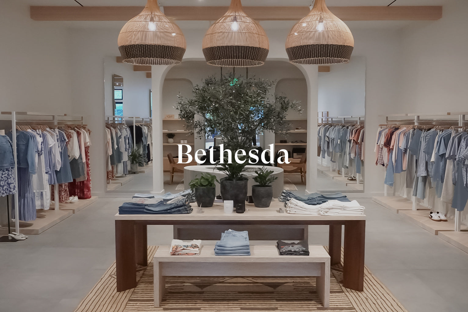 INSIDE OF BETHESDA STORE SHOWING MULTIPLE RACKS OF CLOTHING ALONG EACH WALL AND A TABLE IN THE CENTER OF THE ROOM