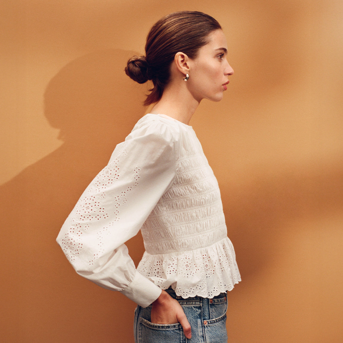 Woman wearing a white lace top against an orange background