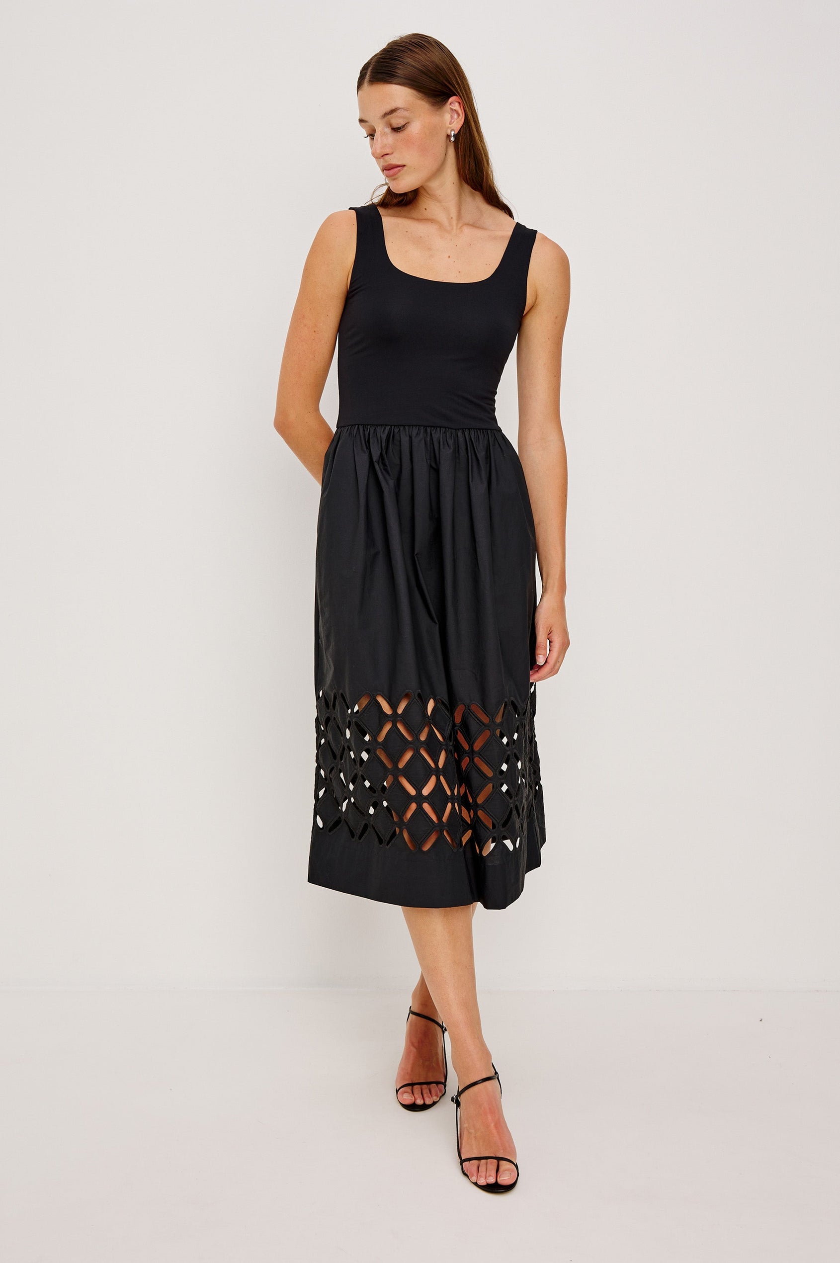 Nadya is a midi dress with a soft scoop neck bodice and a lightweight skirt in Black Colorway. The skirt features engineered cutouts from mid-thigh to hem and includes discreet on-seam pockets. Full Body front view featured on model.