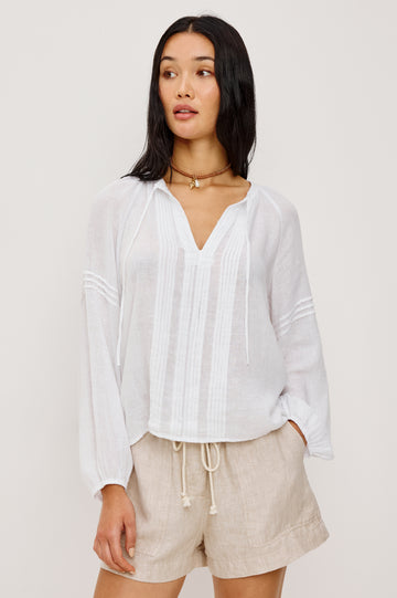 Naples Top in Linen With Split V-Neckline With Self-Ties Long Billowing Sleeves With Fitted Cuffs Loose SIlhouettes and Intricate Seam Detailing in White Colorway - Upper Body Front View Featured on Model