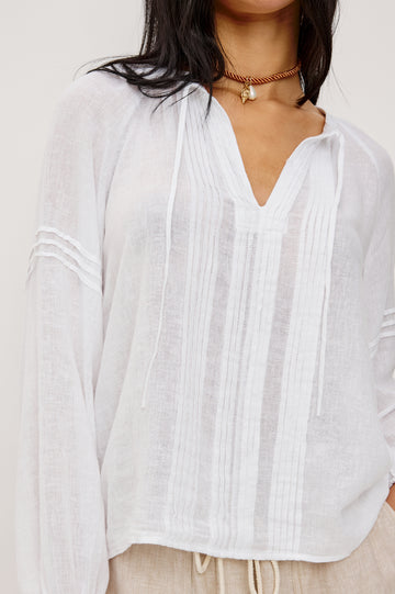 Naples Top in Linen With Split V-Neckline With Self-Ties Long Billowing Sleeves With Fitted Cuffs Loose SIlhouettes and Intricate Seam Detailing in White Colorway - Upper Body Close Up Front View Featured on Model