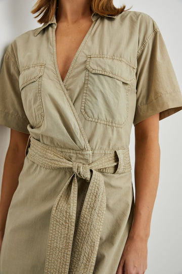 Natalie Short Sleeve Mini Dress with a Deep V Neck, Fabric Tie Belt, Belt Loops, Two Chest Flap Pockets, Buttoned Horizontal Flap on the Back and a Collar in Olive Colorway - Front View Featured on Model 