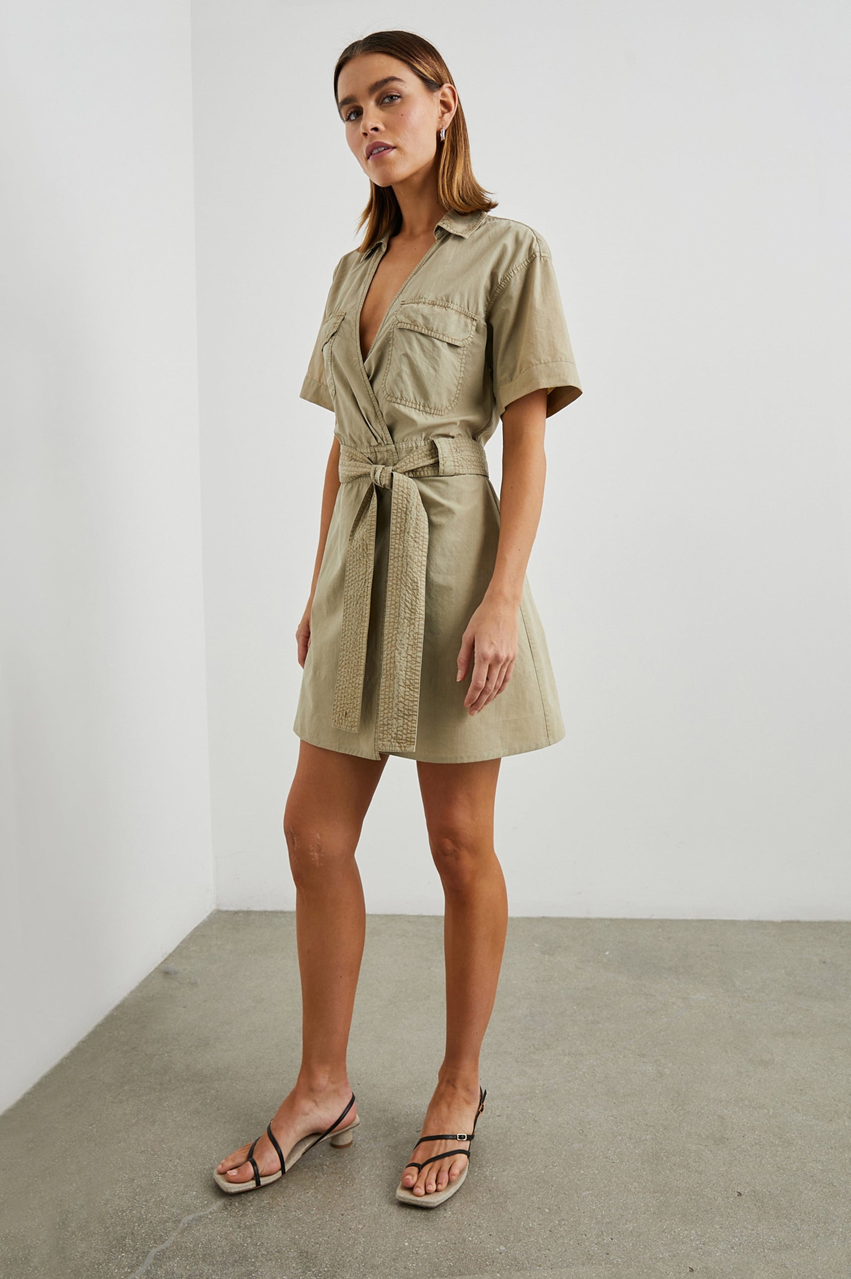 Natalie Short Sleeve Mini Dress with a Deep V Neck, Fabric Tie Belt, Belt Loops, Two Chest Flap Pockets, Buttoned Horizontal Flap on the Back and a Collar in Olive Colorway - Front Full Body View Featured on Model 